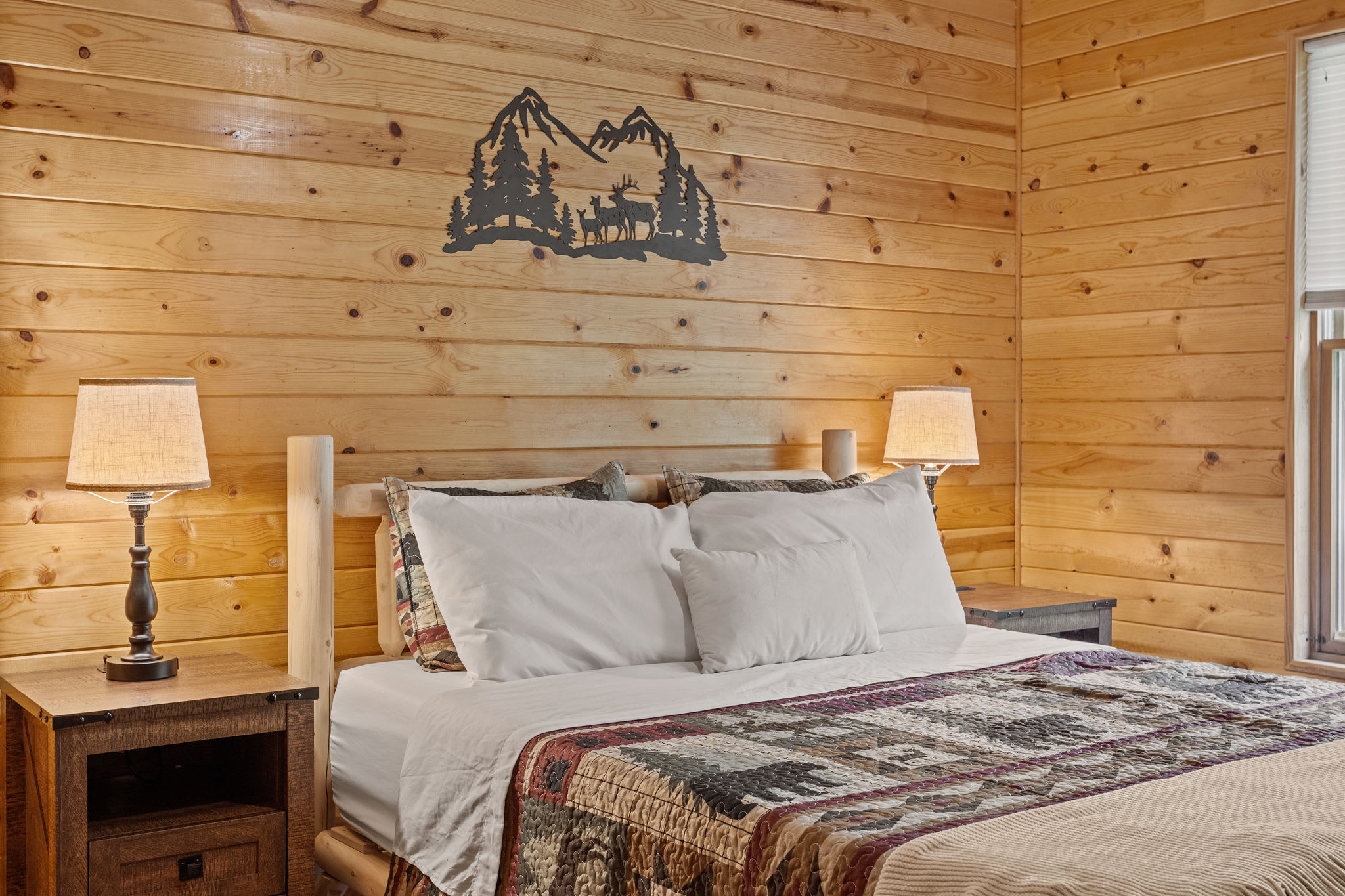A cozy bed adorned with cabin-inspired bedding, soft lighting, and natural wood surroundings make this space a peaceful retreat.