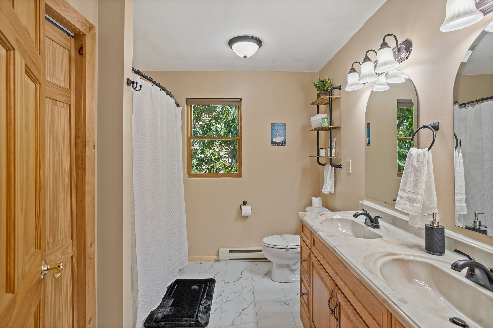 This full bathroom boasts a modern yet rustic design, with a large window, cozy lighting, and a shower.