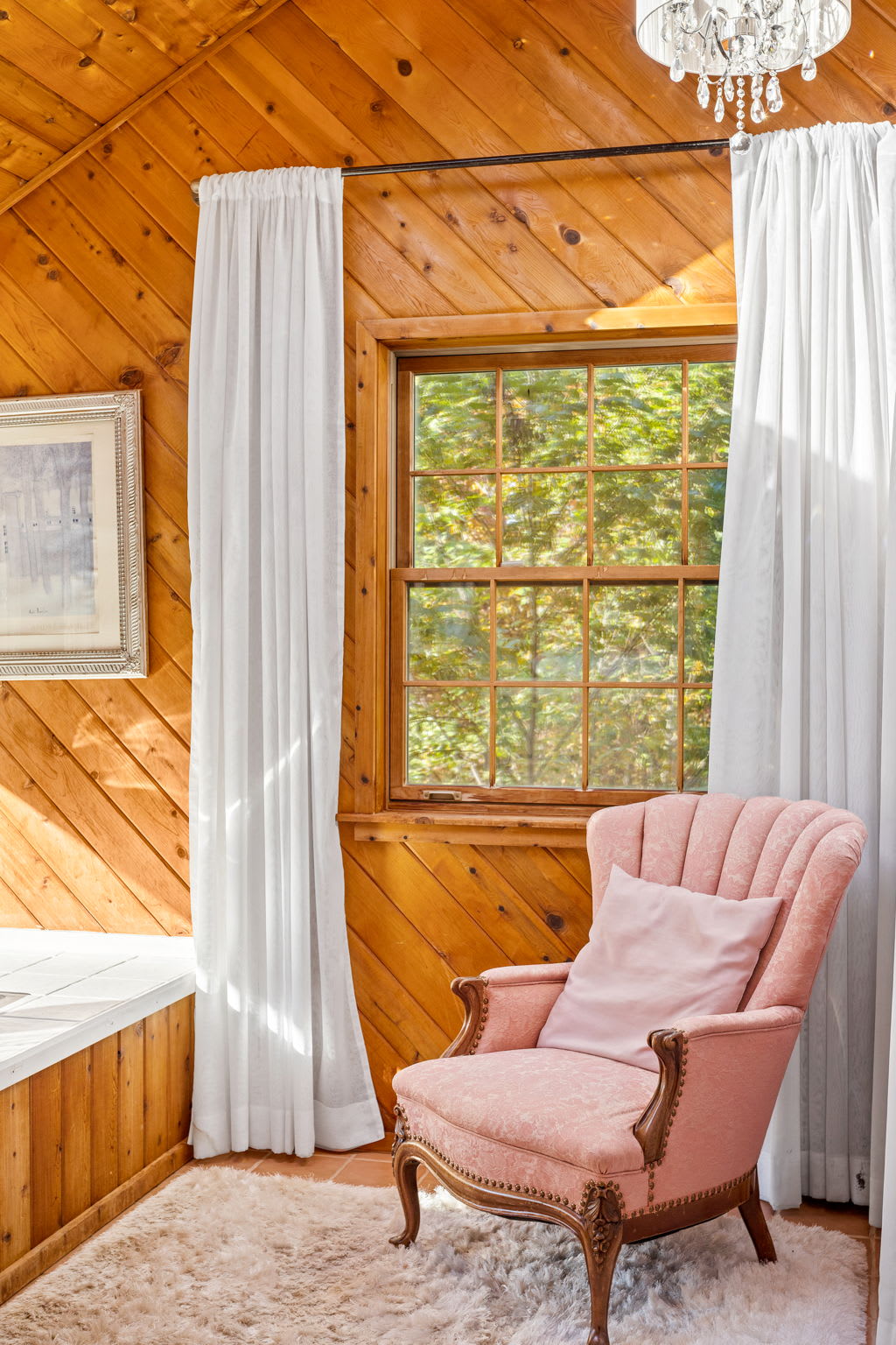 A plush pink chair and soft rug add a romantic, vintage charm to the sunlit soaking area.