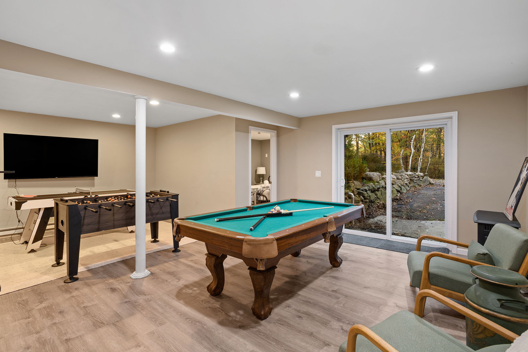 A bright game room with a classic pool table takes center stage, complemented by foosball and a wide-open view to the outdoors.