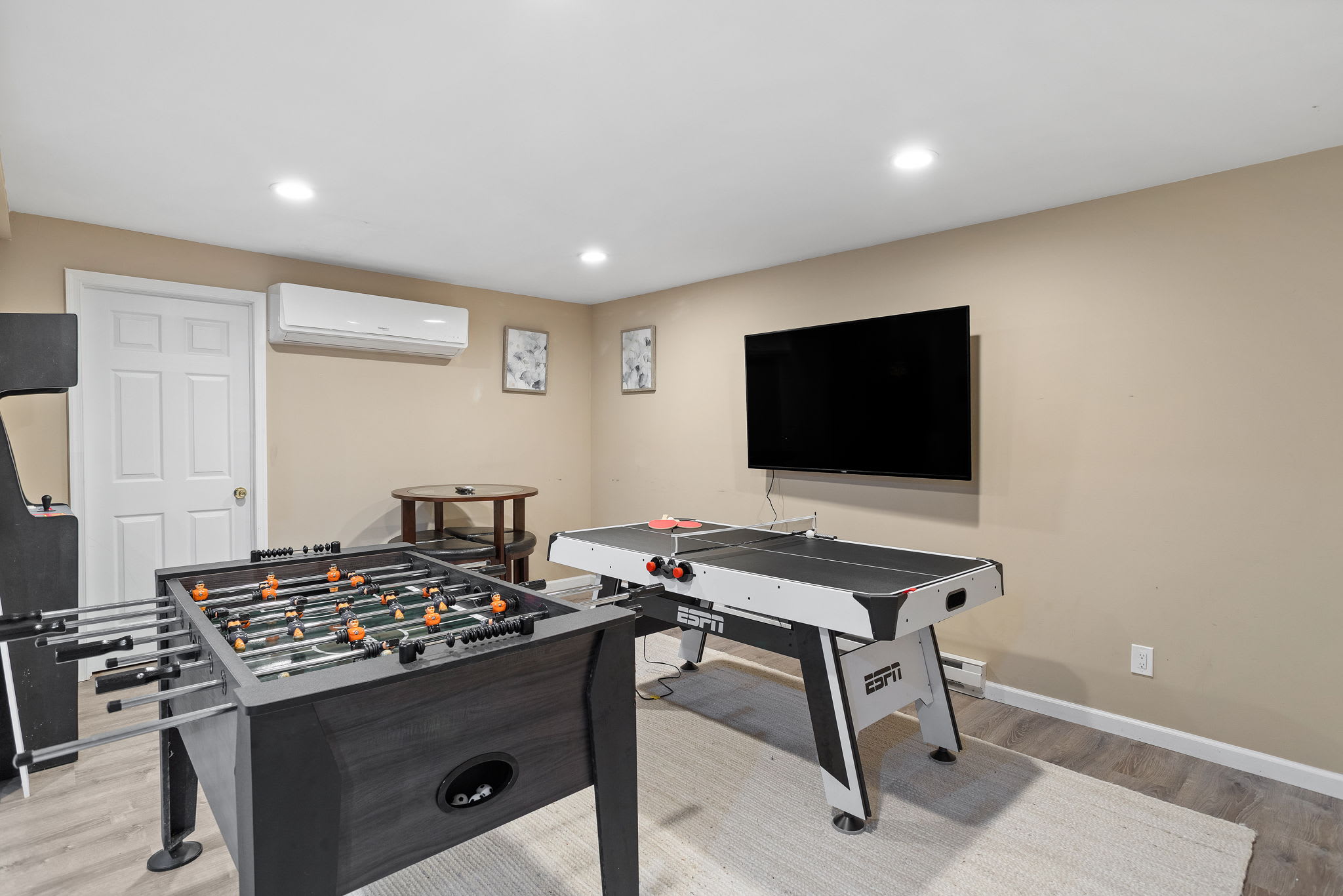 A large TV stands ready for entertainment, with foosball and an all-in-one game table offering endless fun for guests.