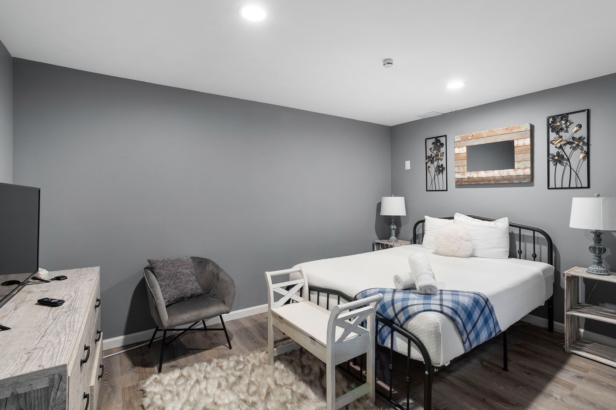 A contemporary guest room with a metal-frame bed, cozy linens, and soft gray walls, perfect for winding down after game night.