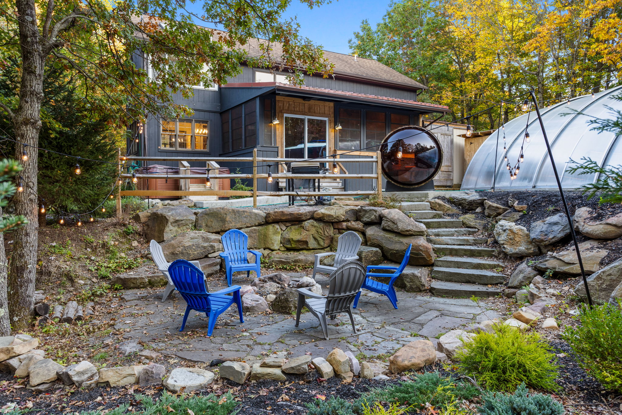 Surrounded by lush foliage, a stone fire pit area invites you to gather under the stars, complete with Adirondack chairs and a cozy ambiance.