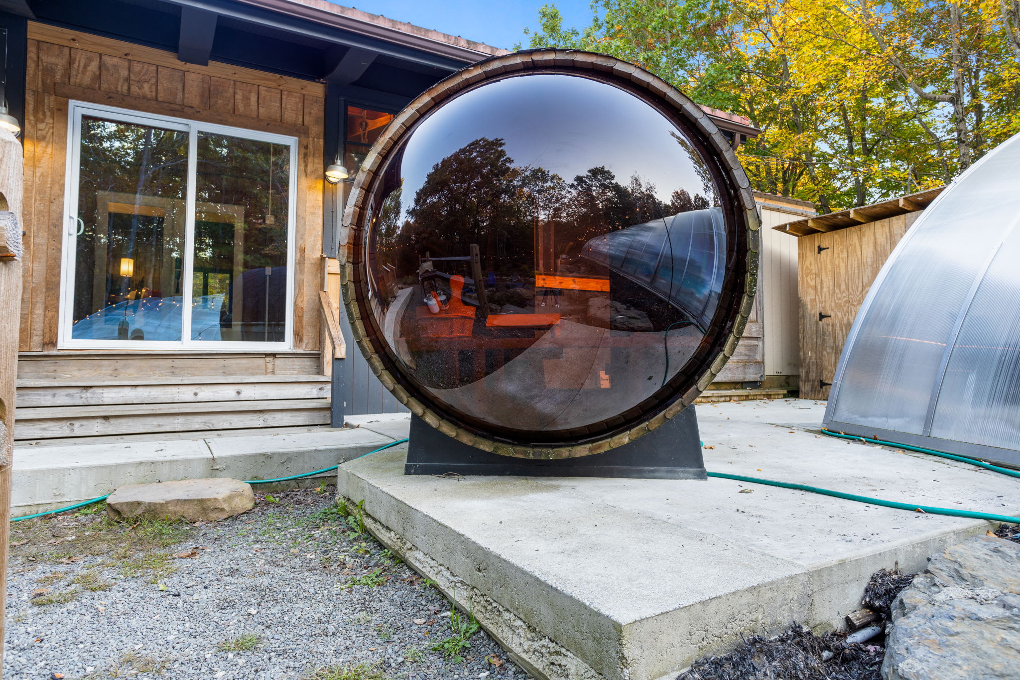 From the outside, the barrel sauna looks like a charming wooden orb. Its tinted glass front provides a cozy glow inside while blending seamlessly into the natural setting.