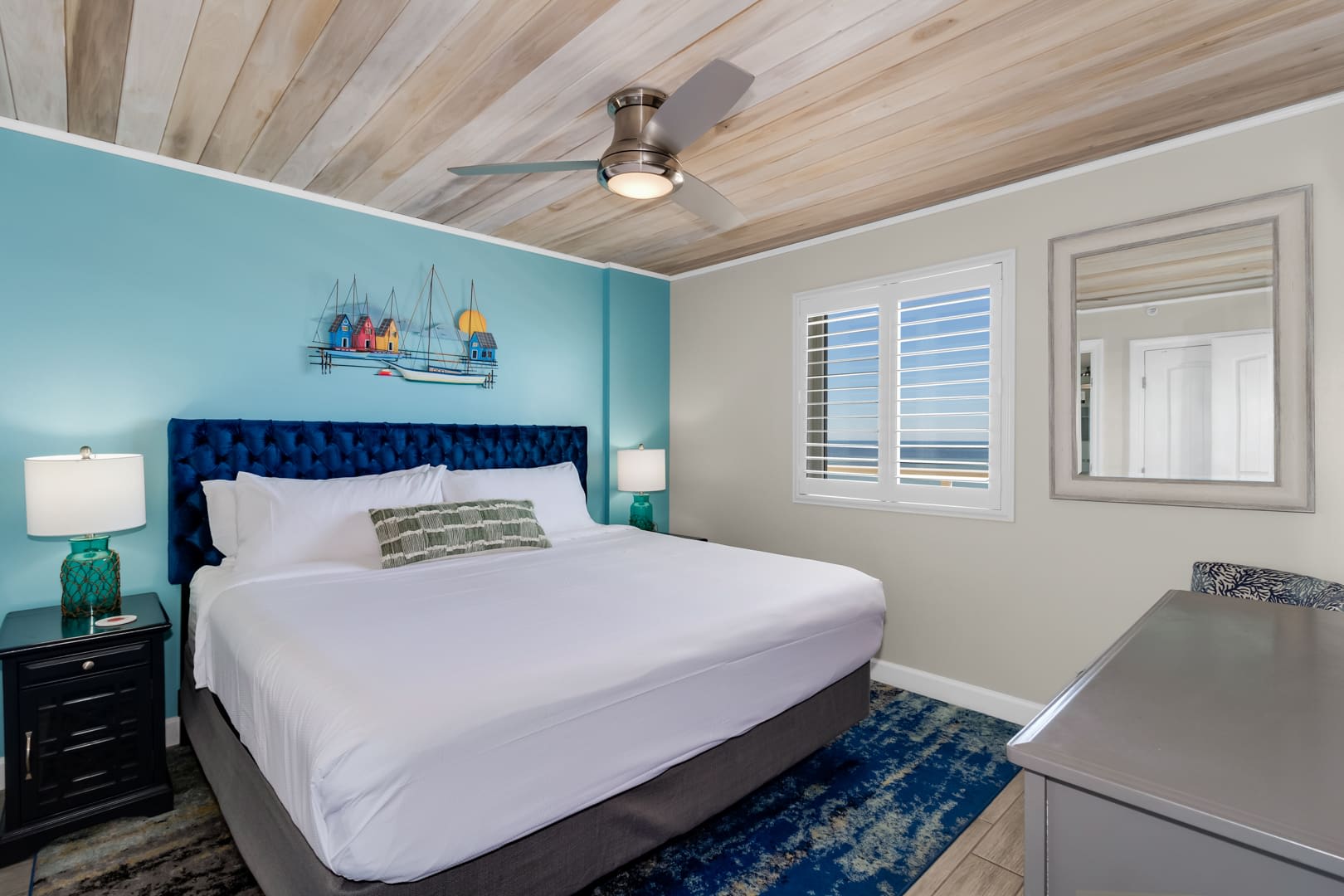 Unwind in this cozy bedroom featuring a plush king-sized bed, nautical-inspired decor, and a ceiling fan for added comfort. Wake up refreshed with natural light and glimpses of the ocean just outside your window—your perfect seaside retreat!