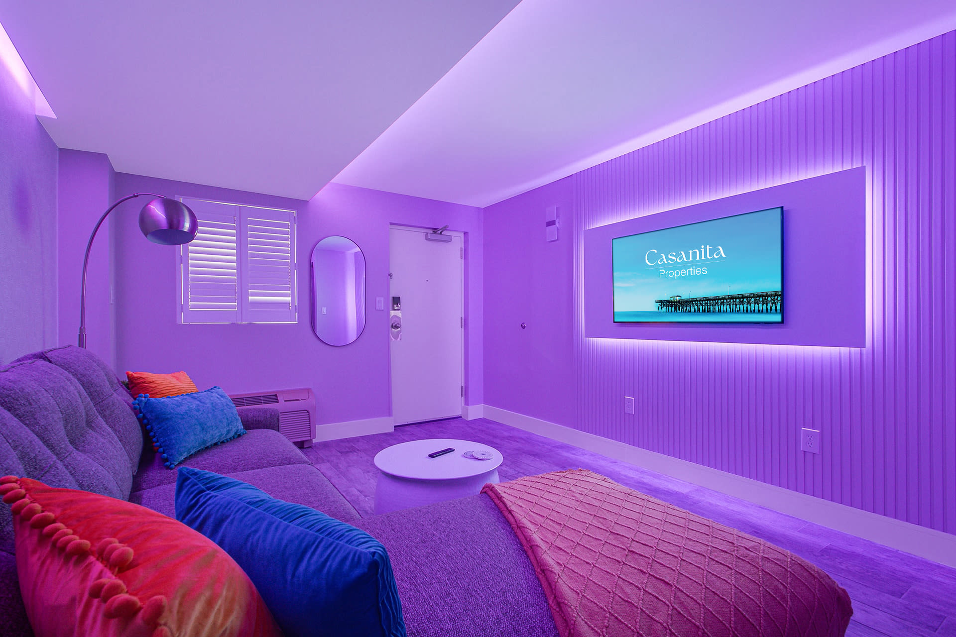 Enhanced by ambient purple lighting that sets a relaxing mood. The cozy sectional, modern decor, and wall-mounted TV create an inviting atmosphere, perfect for evening relaxation or movie nights in style.