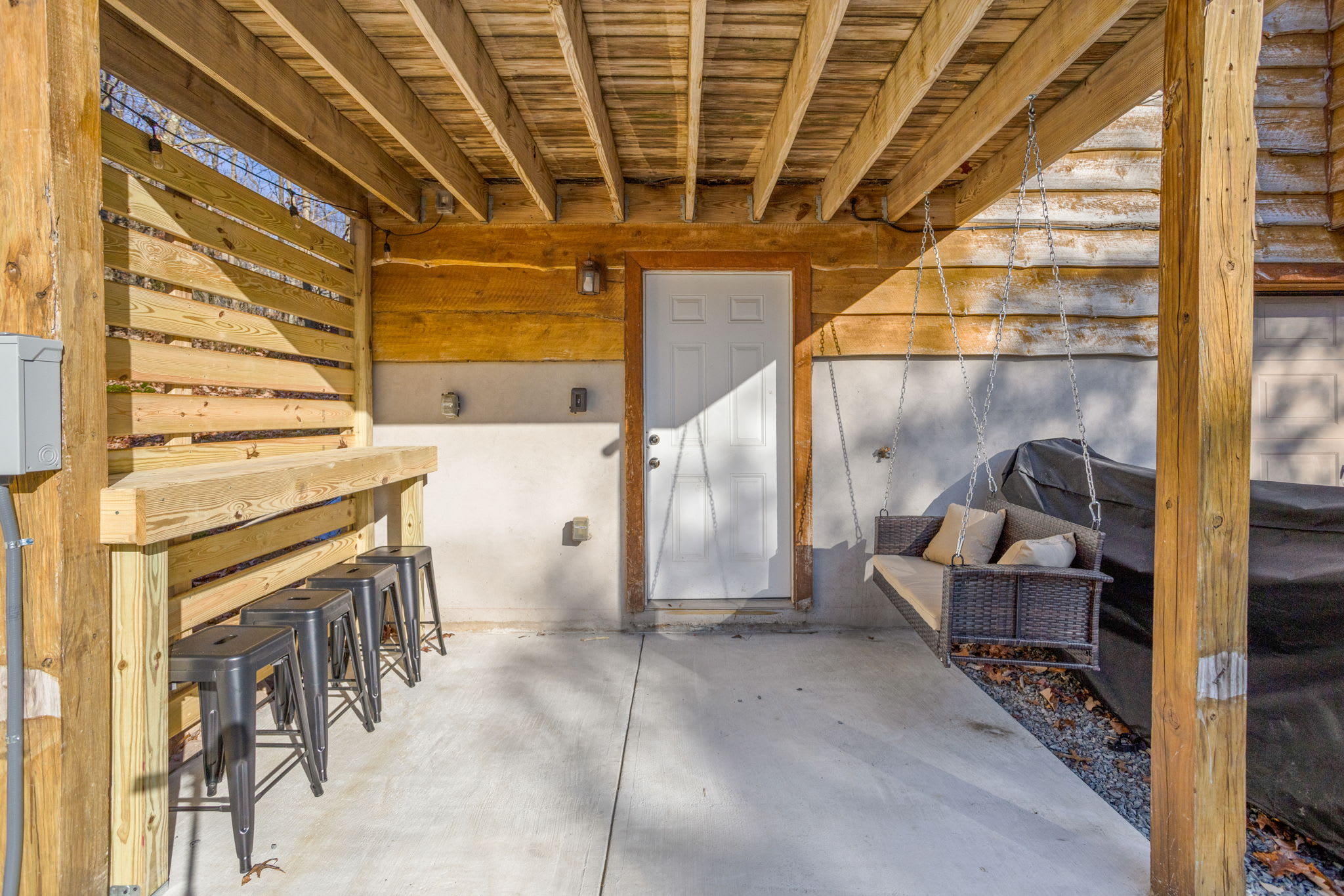 A stylishly designed covered patio with a bar area and a hanging swing, creating a relaxing spot to unwind.