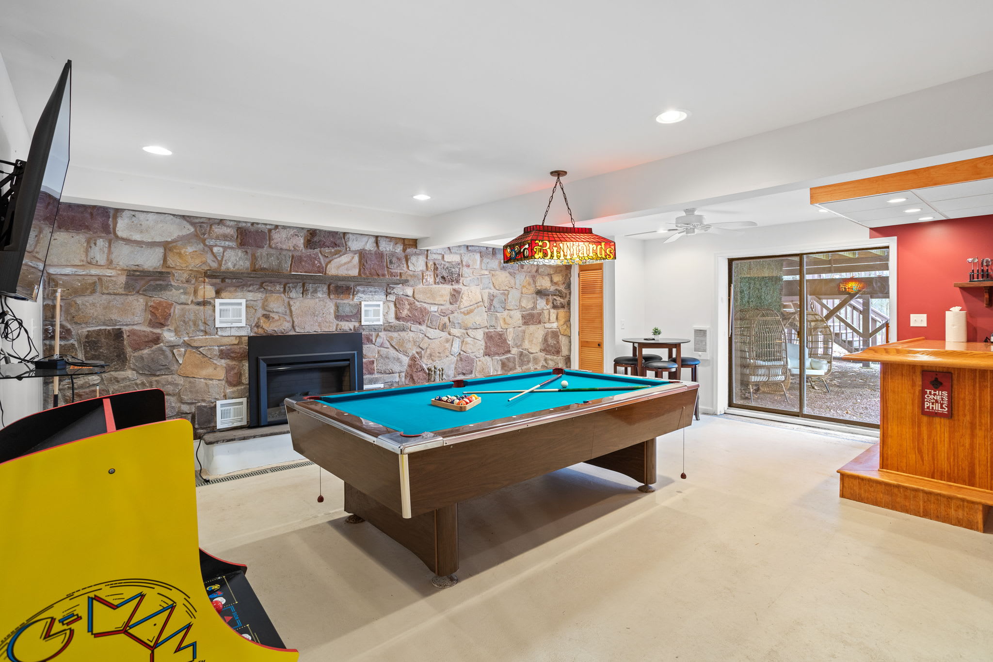 This spacious entertainment room features a pool table, arcade games, a fireplace, and a warm, inviting atmosphere.