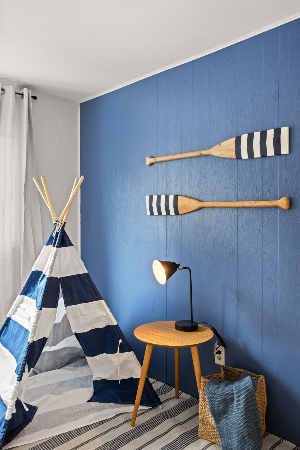 Oars mounted on a bold blue accent wall add a unique touch to this themed bedroom. A cozy side table and lamp complete the inviting atmosphere.