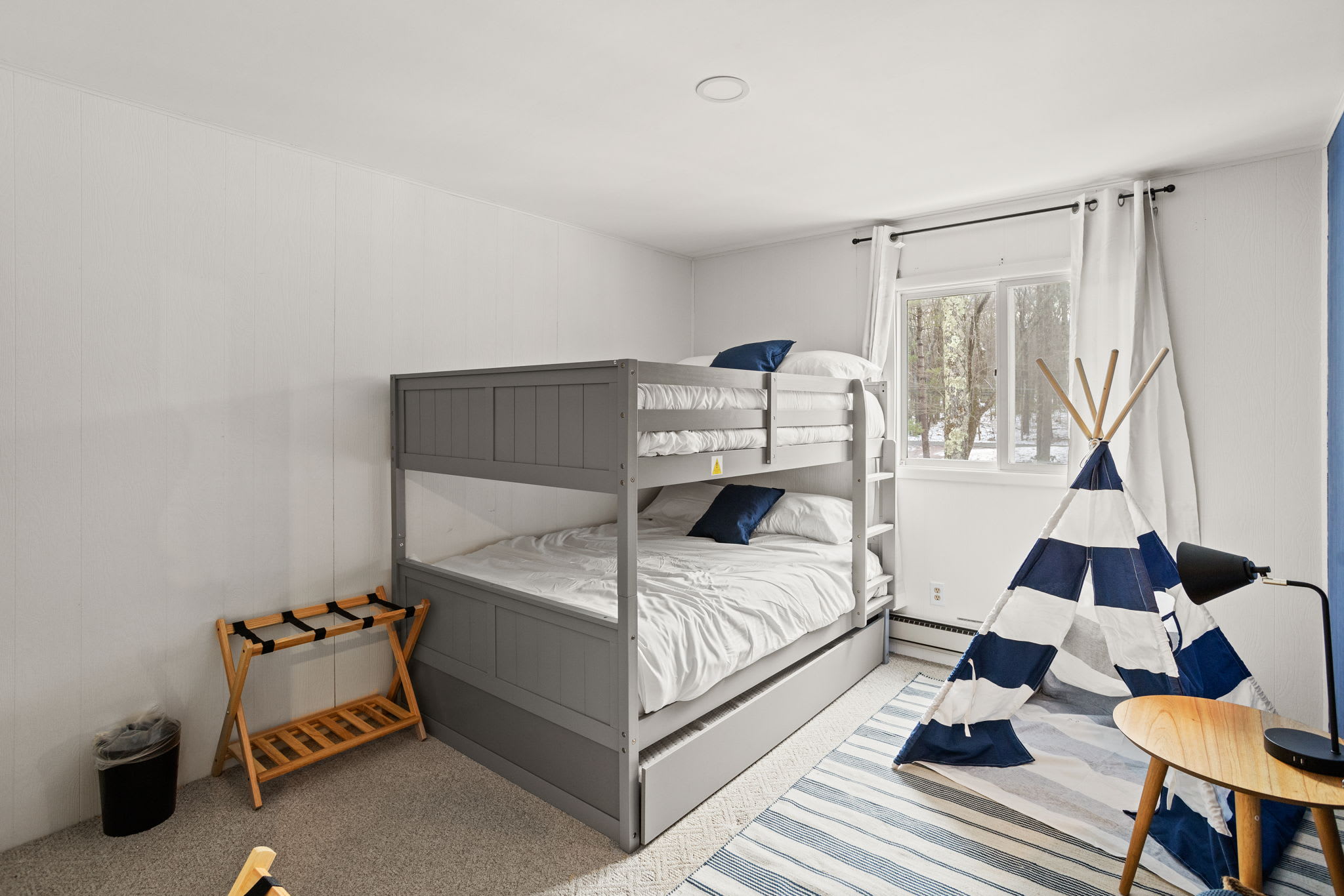 This thoughtfully designed bedroom features sturdy gray bunk beds, a stylish navy and white teepee, and plenty of natural light. A fun and functional space for little adventurers or group stays. (1 Bunk Bed with 1 single pull-out bed under)