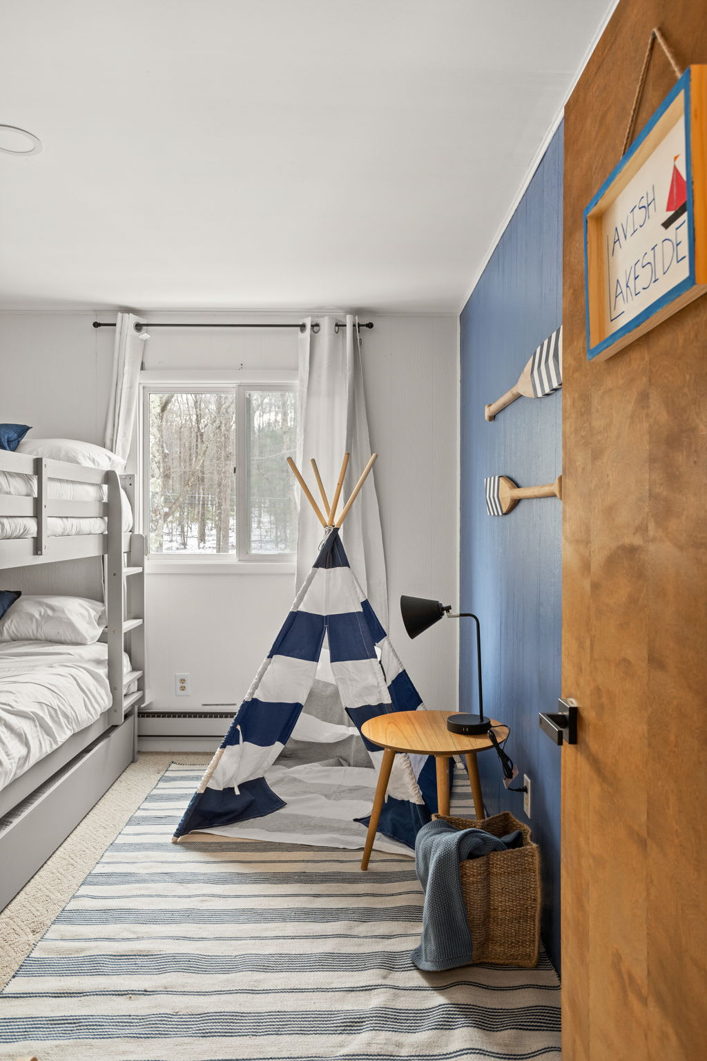 A well-lit bedroom with soft blue and neutral tones, striped rugs, and a cozy teepee corner for relaxation or playtime. The perfect blend of comfort and charm.