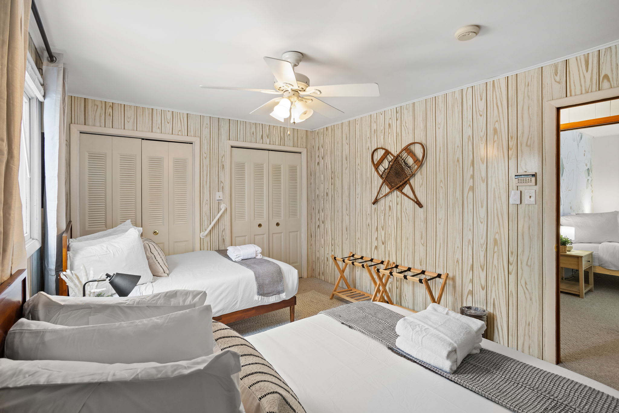 A cozy, well-lit bedroom with charming wood-paneled walls, soft linens, and large windows that bring in plenty of natural light. (2 Queen Size Bed)