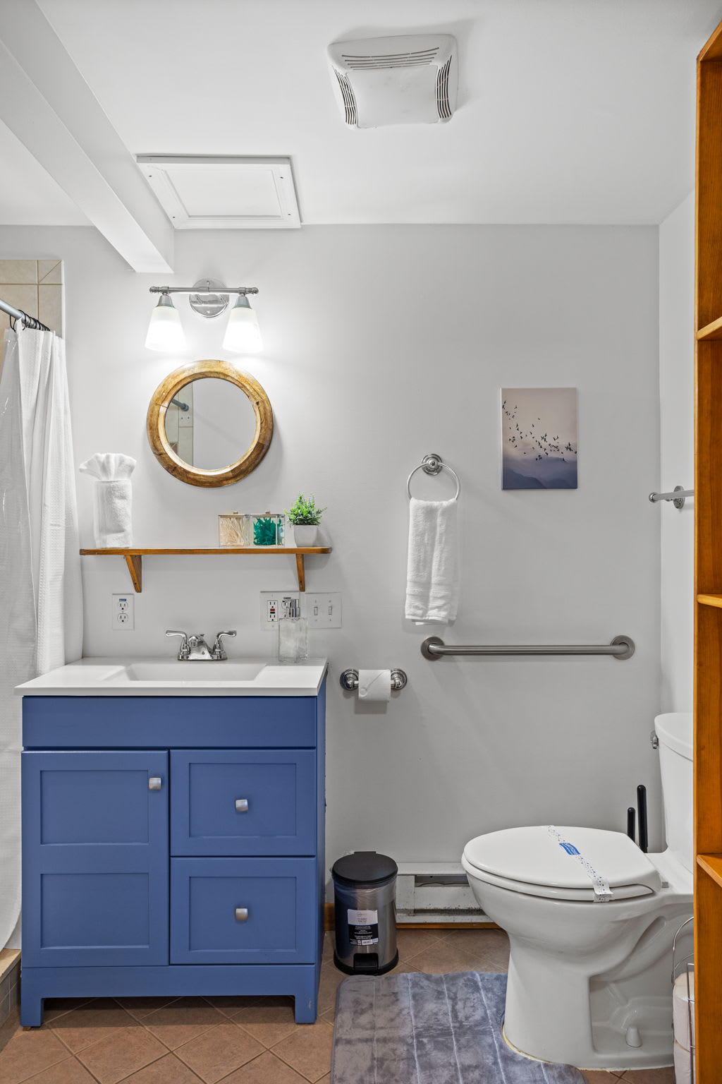A bright and inviting bathroom with stylish blue cabinetry, a circular mirror, and a spa-like shower setup. A perfect mix of comfort and convenience.