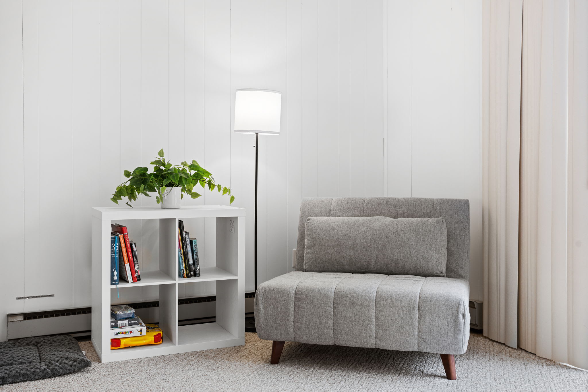 A quiet corner featuring a chic accent chair, a stylish book collection, and a soft-lit floor lamp.