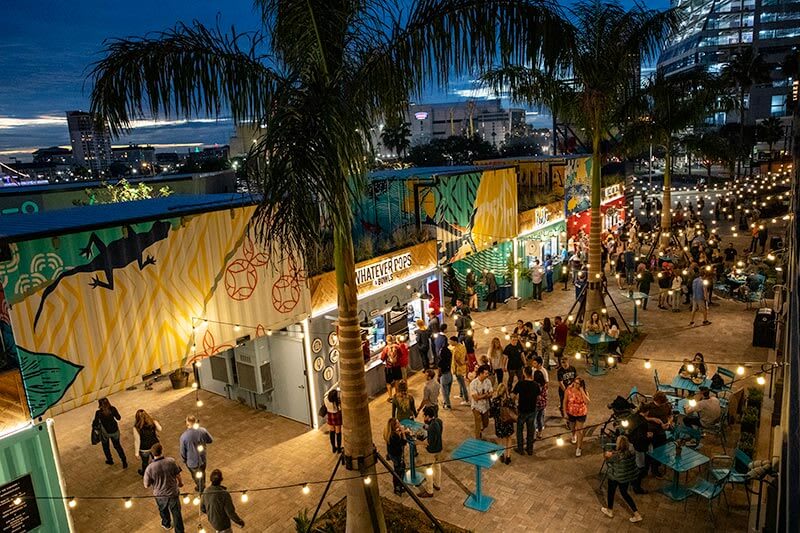 Lively outdoor plaza at night w/ lights and a buzzing atmosphere.