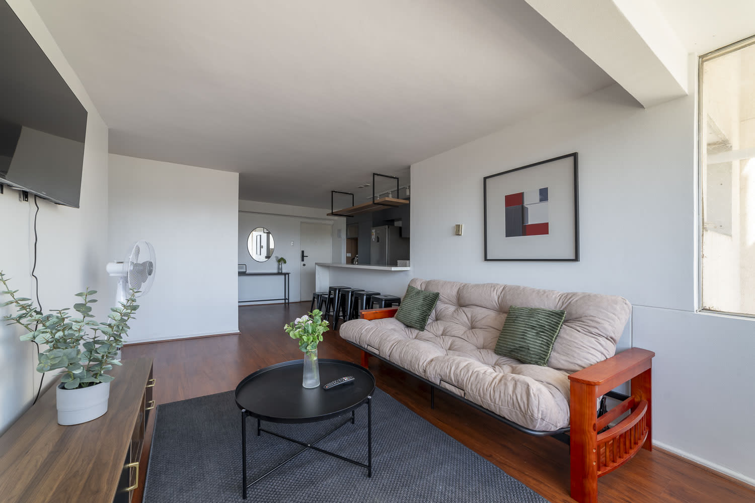 Relax in this modern living room with a cozy futon, stylish decor, and a seamless flow into the kitchen area.