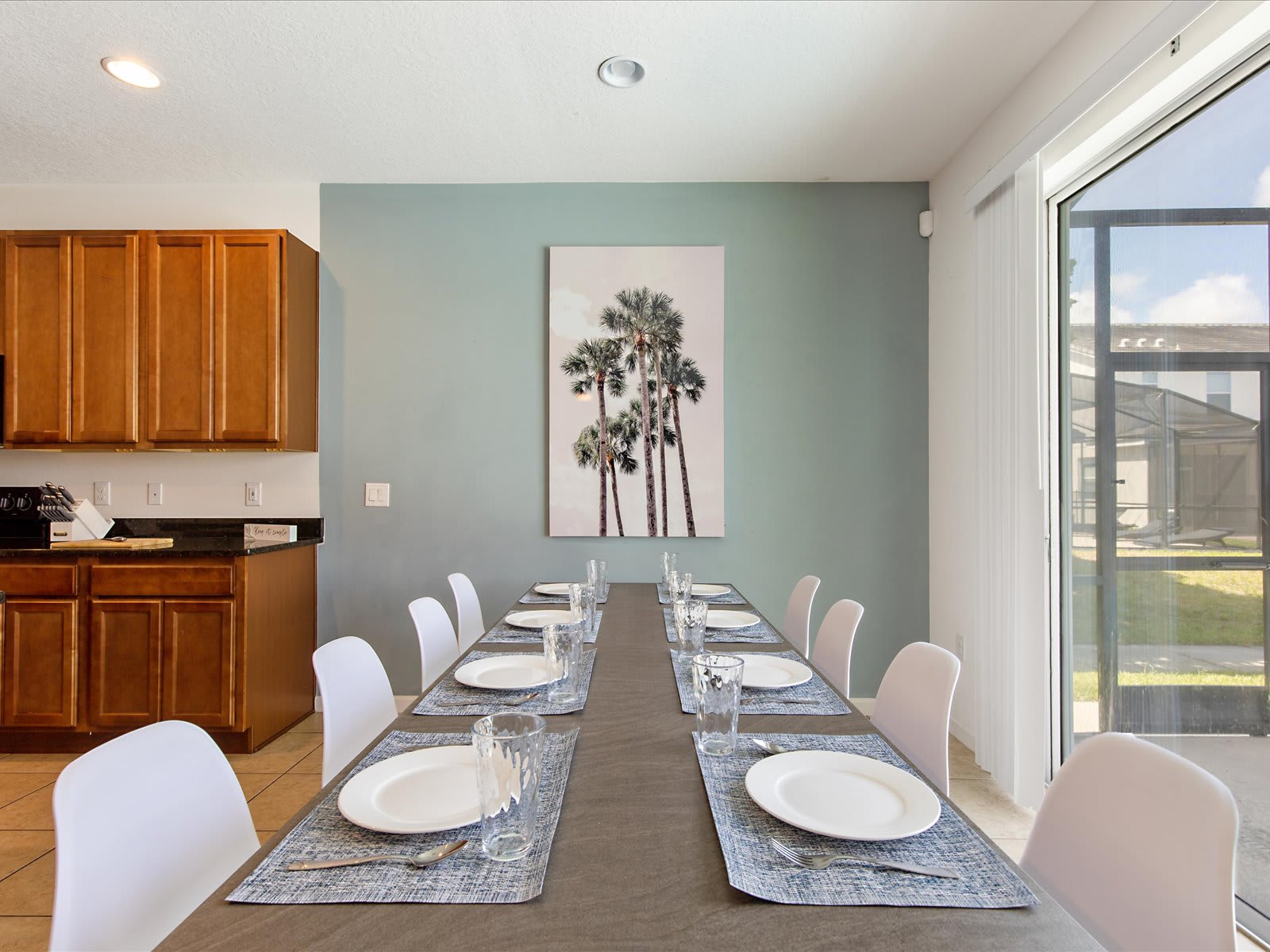 Sunlit dining table set for group meals beside sliding glass doors.