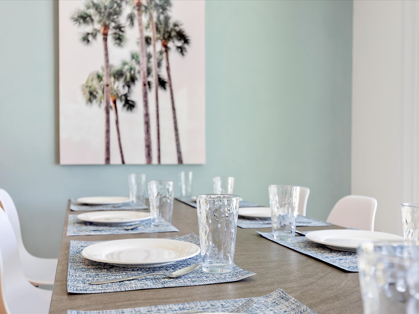 Stylish dining setup w/ simple place settings & calm coastal artwork.