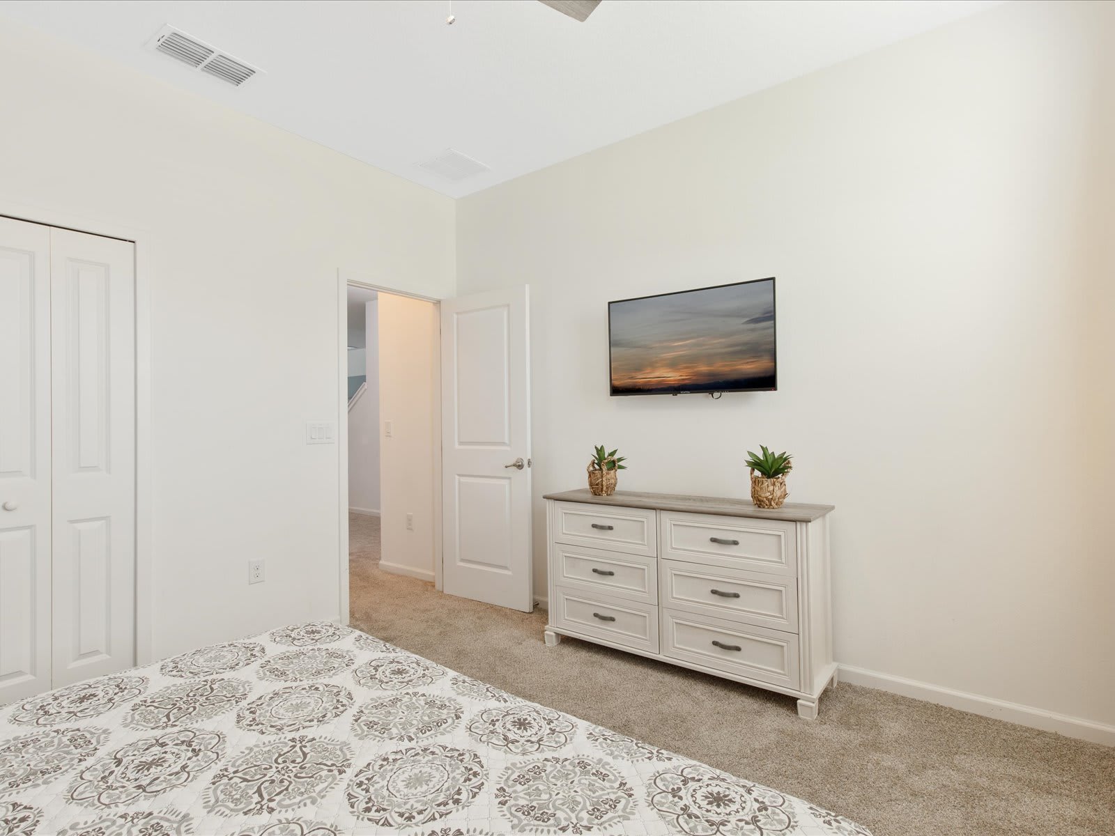 Comfortable bedroom w/ dresser, TV, & soft, neutral tones.