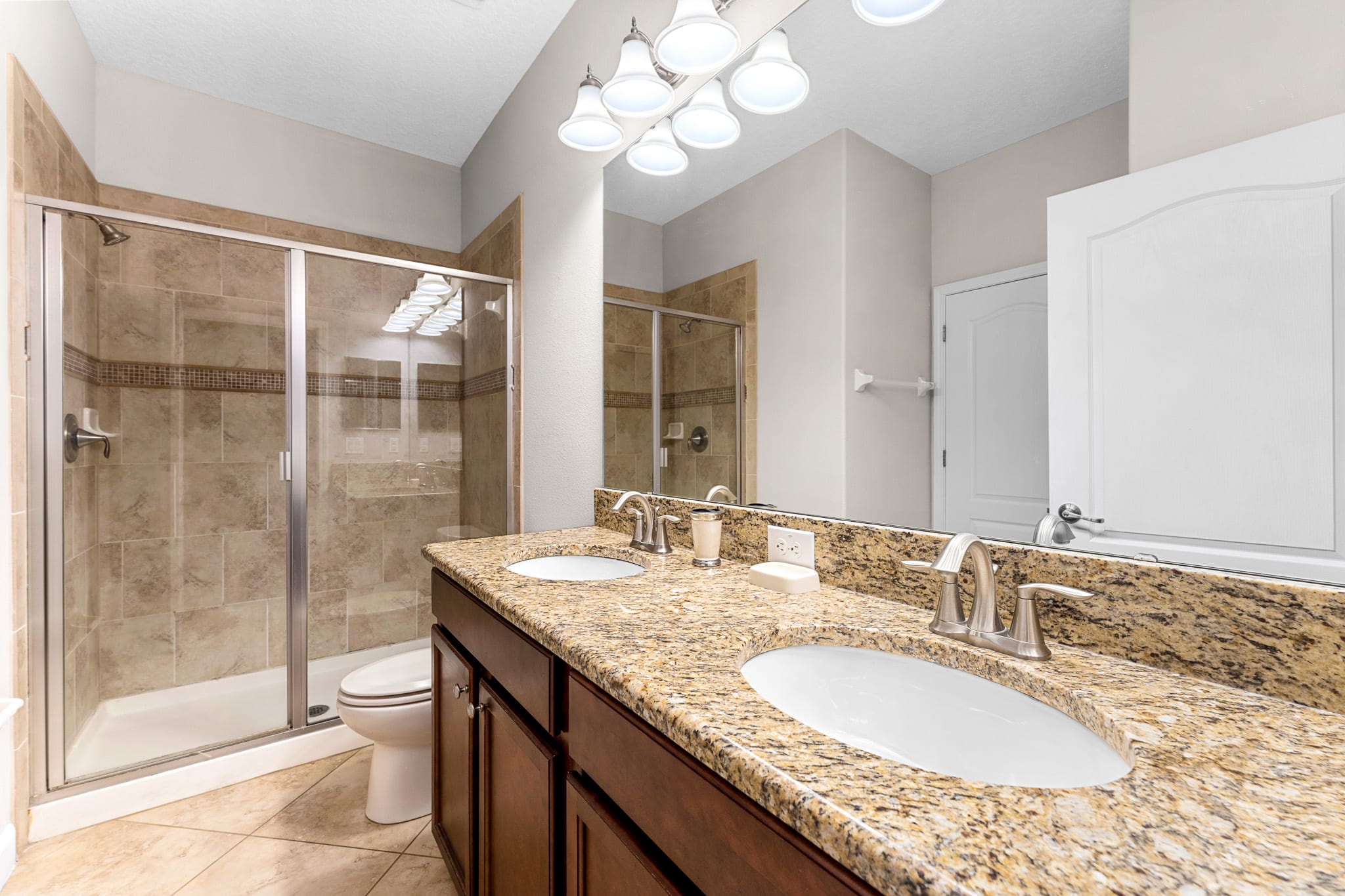 Spacious bathroom w/ wide mirror, sink, and glass-enclosed shower.