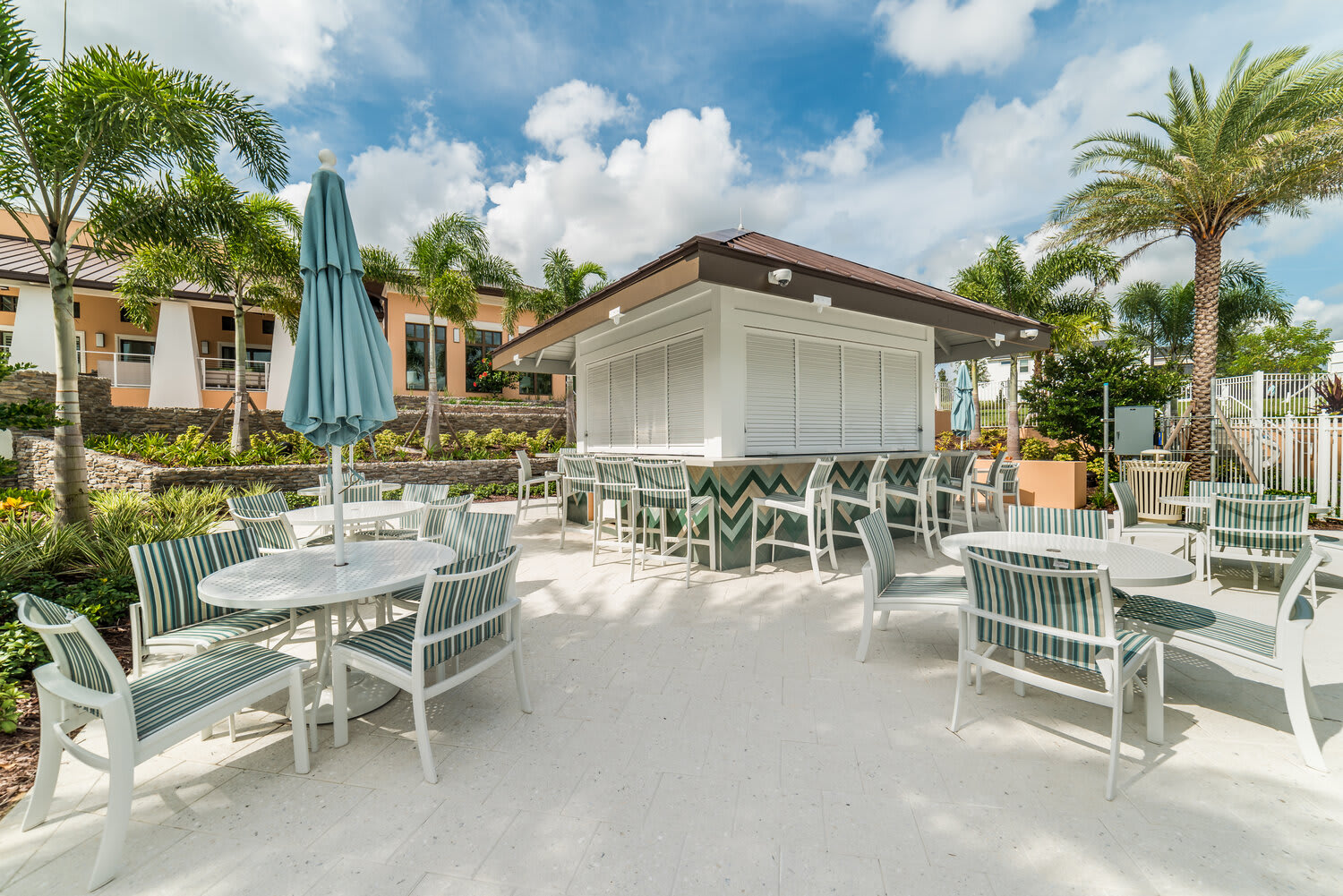 Outdoor seating area with striped chairs and a shaded bar under a bright sky