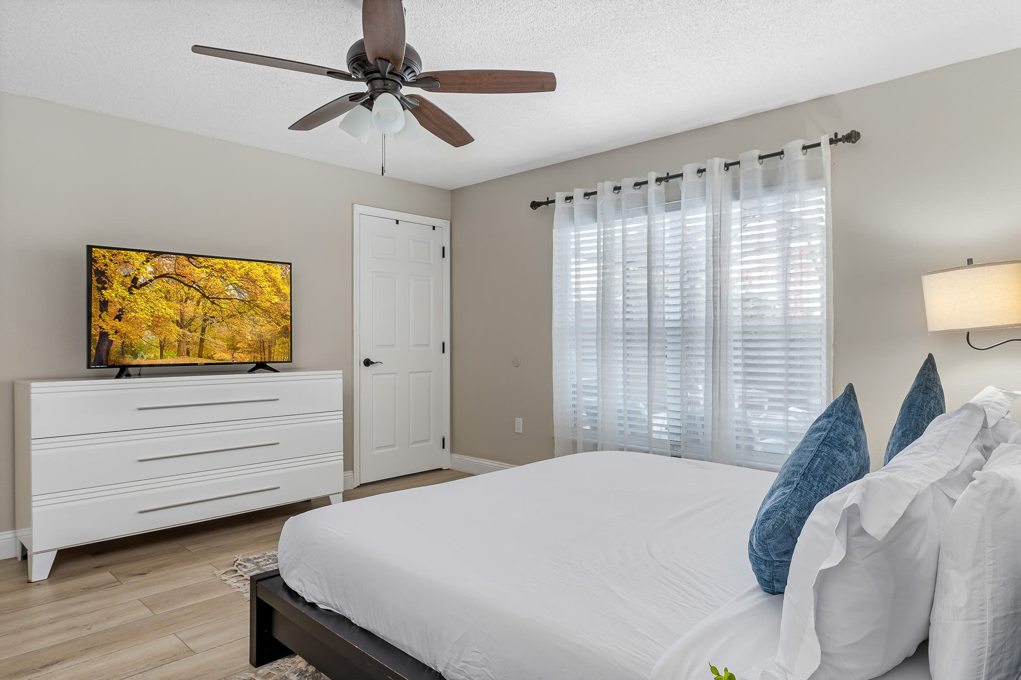 Cozy bedroom w/ ceiling fan, bright accents, and natural light from wide windows.