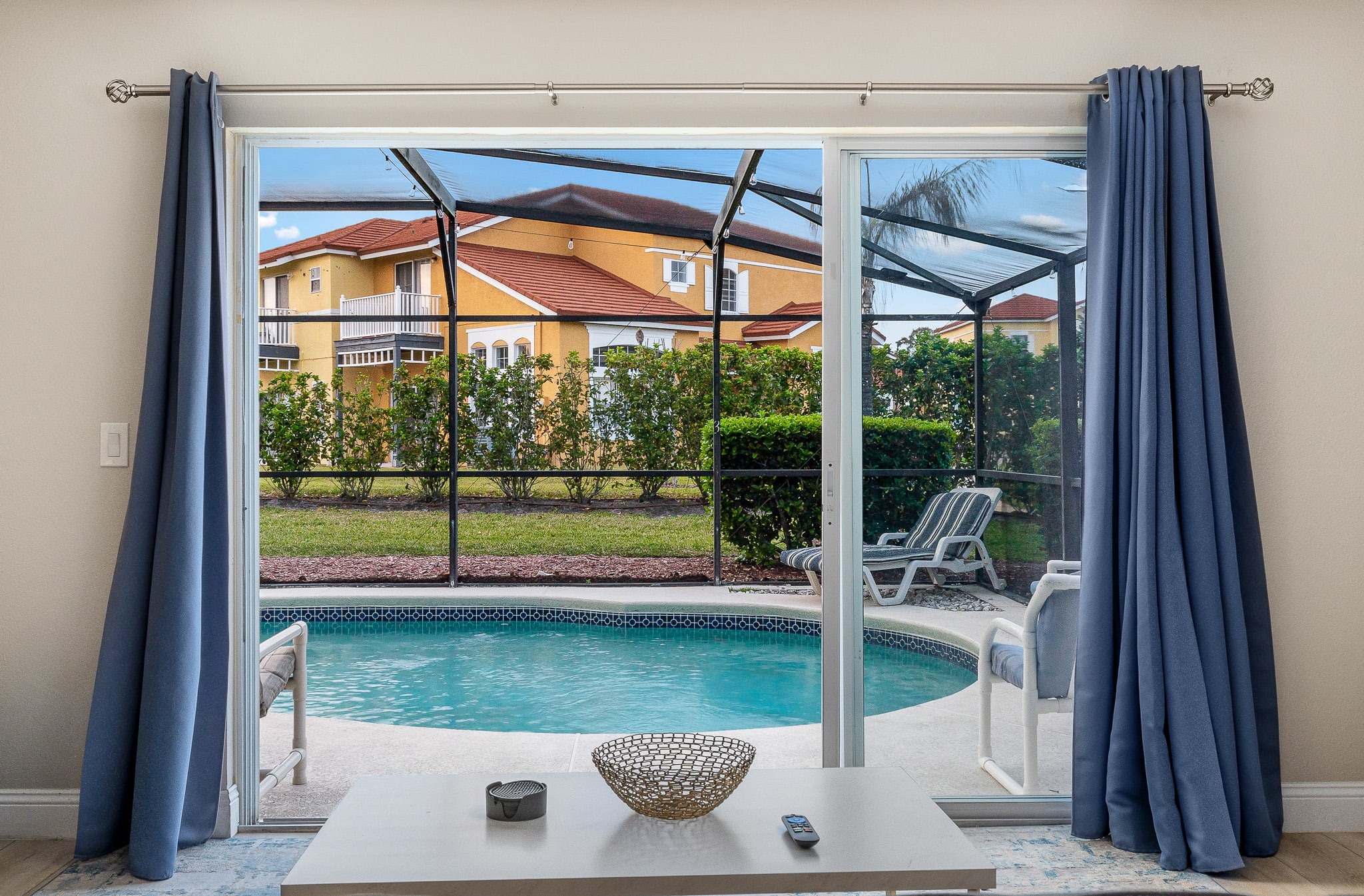 Bedroom view framed by curtains, looking out to lush greenery and blue skies.