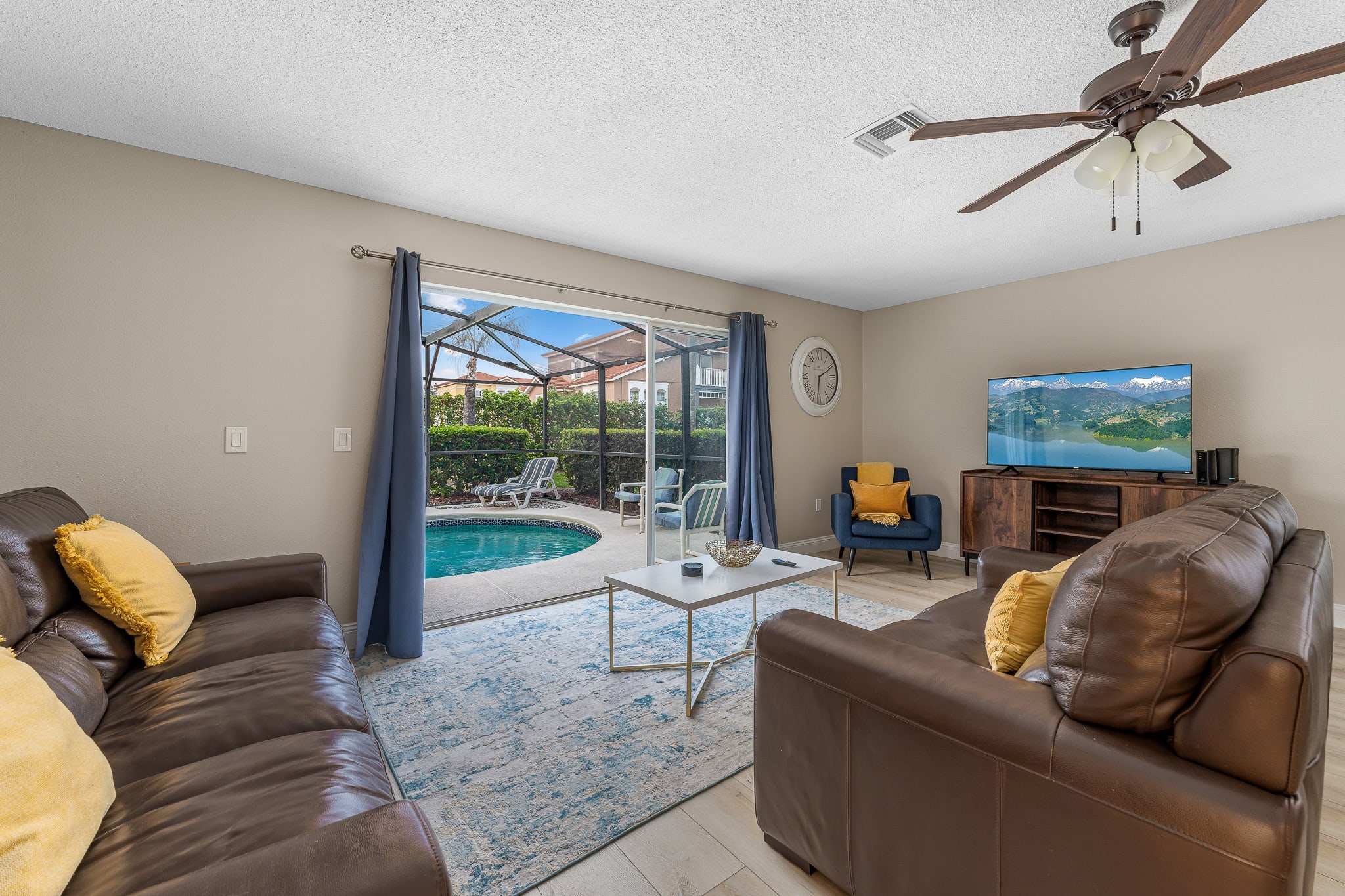 Sunlit living area w/ ceiling fan, cozy sofas, and views to the pool.