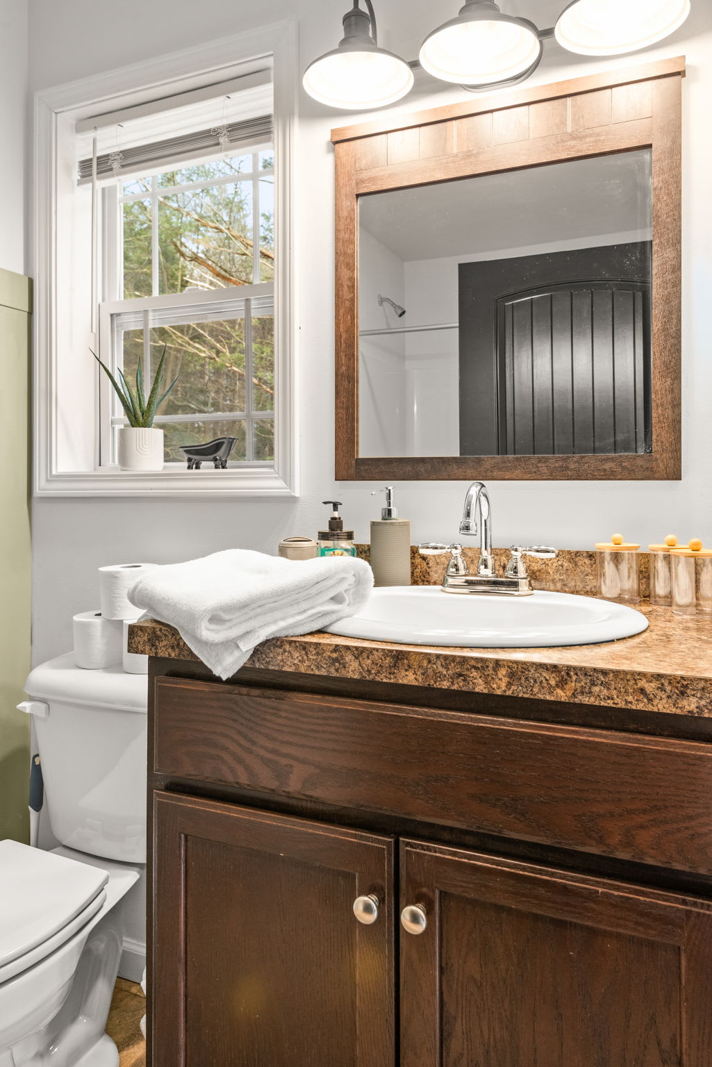 A clean and inviting setup with a well-lit mirror, natural light from the window, and all the essentials you need to freshen up in comfort.