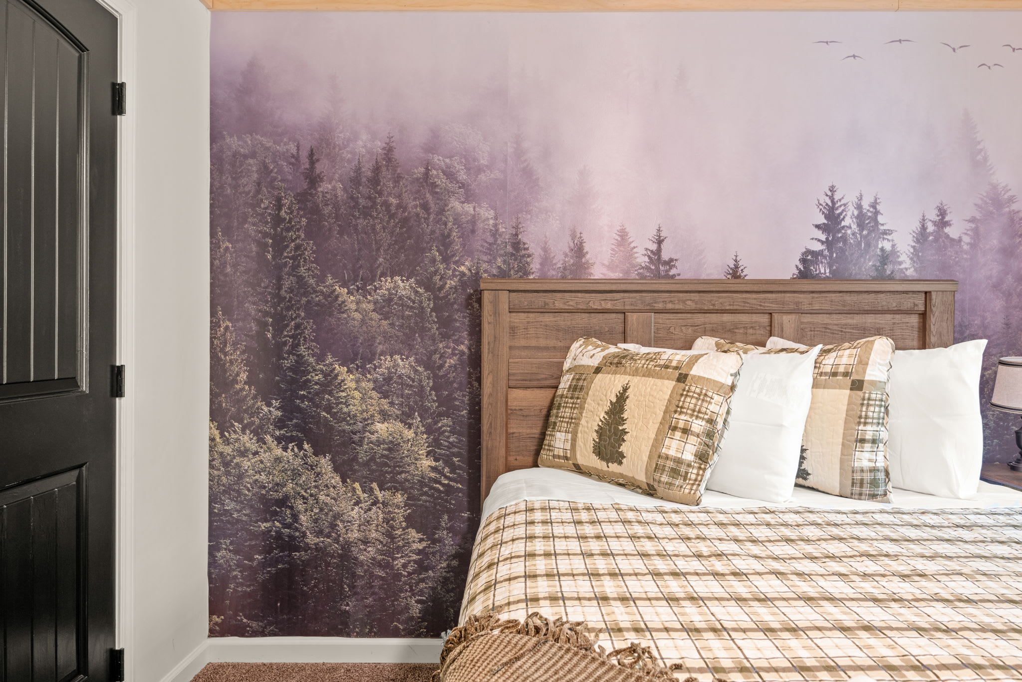 A mural of misty evergreens sets the tone in this whimsical woodland room, paired with plaid bedding and rustic textures for a dreamy mountain vibe.