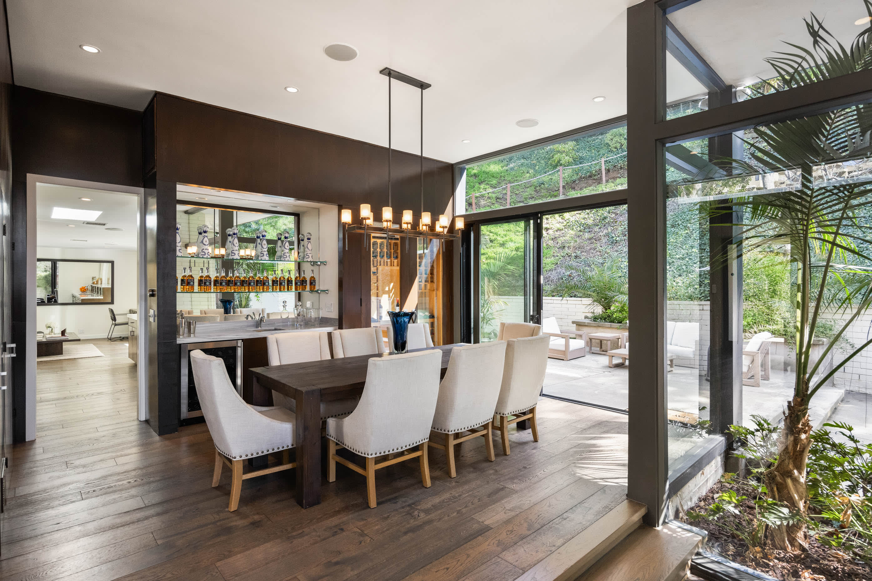 Dine in the stunning dining room surrounded by floor-to-ceiling glass walls, offering views of the lush greenery outdoors.
