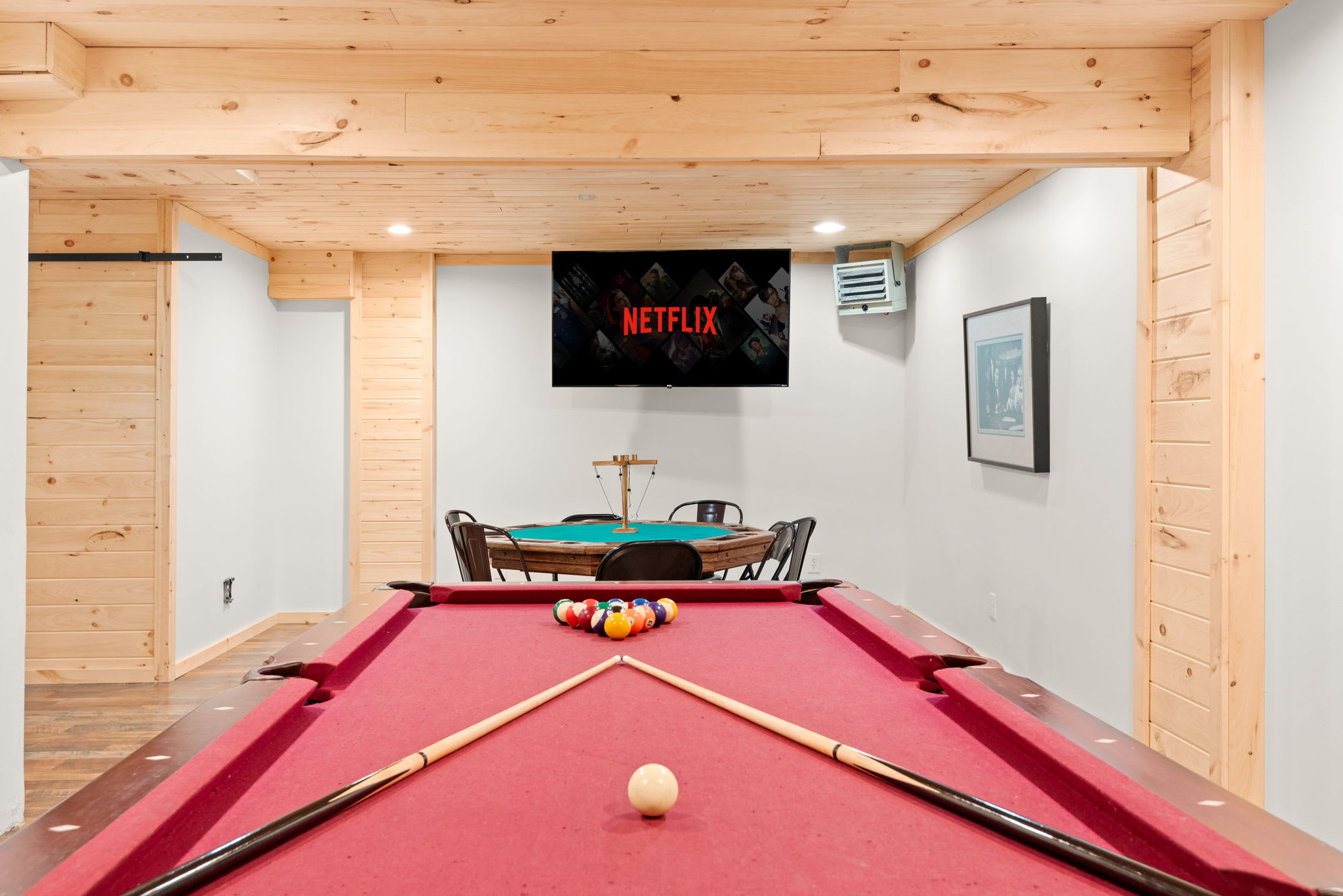 A sleek and inviting entertainment space featuring a red-felt pool table, a poker table, and a mounted TV for endless fun. Whether it's a game of billiards or a poker showdown, this is the perfect hangout spot.