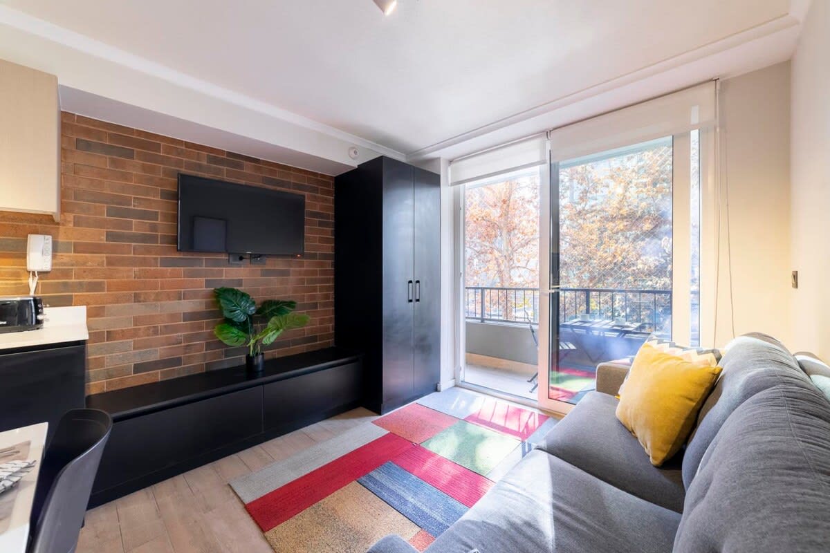 Bright and stylish living area with a cozy sofa, vibrant rug, and balcony access for a refreshing outdoor feel.
