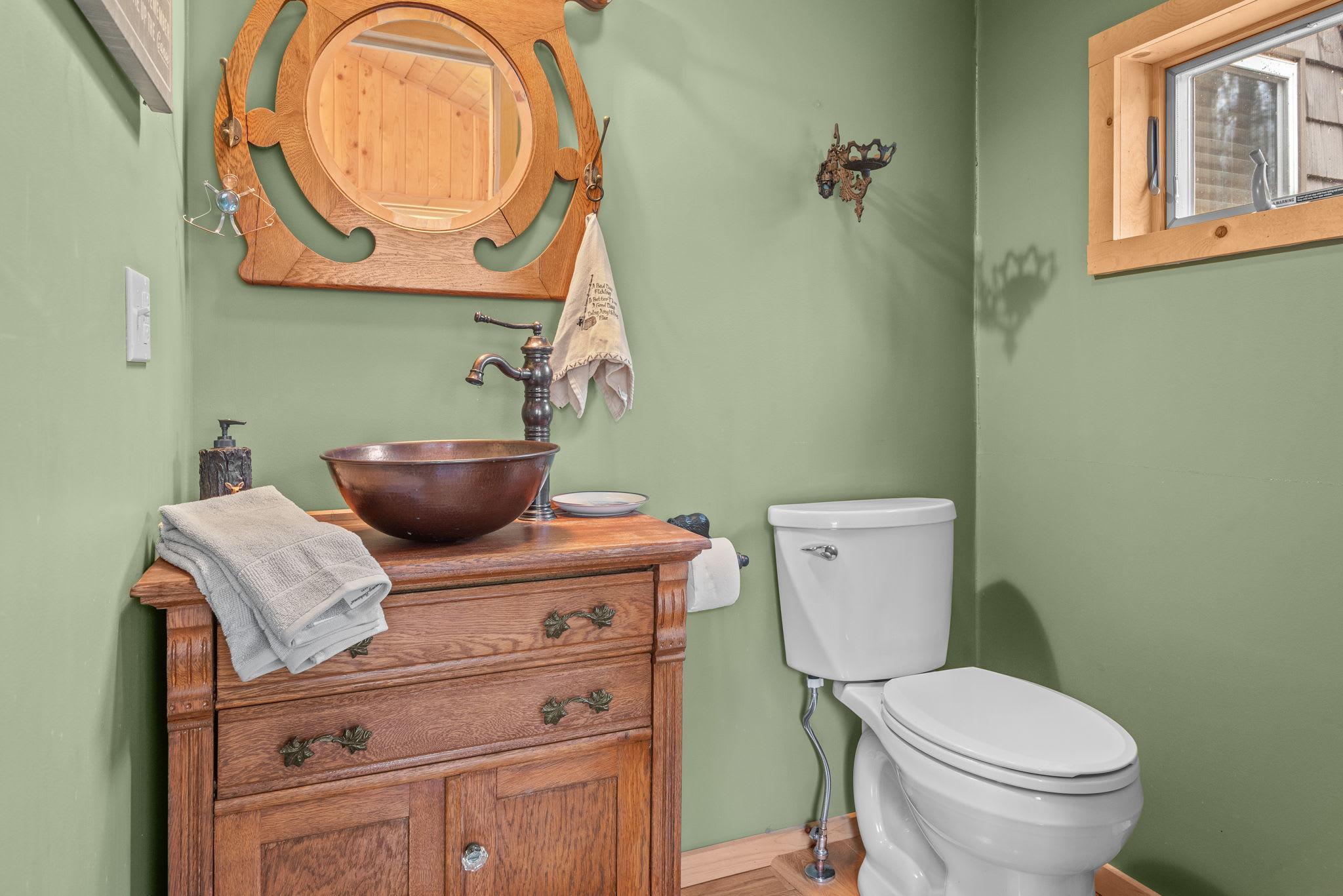 A beautifully designed bathroom with an antique wooden vanity, a copper vessel sink, and nature-inspired decor.
