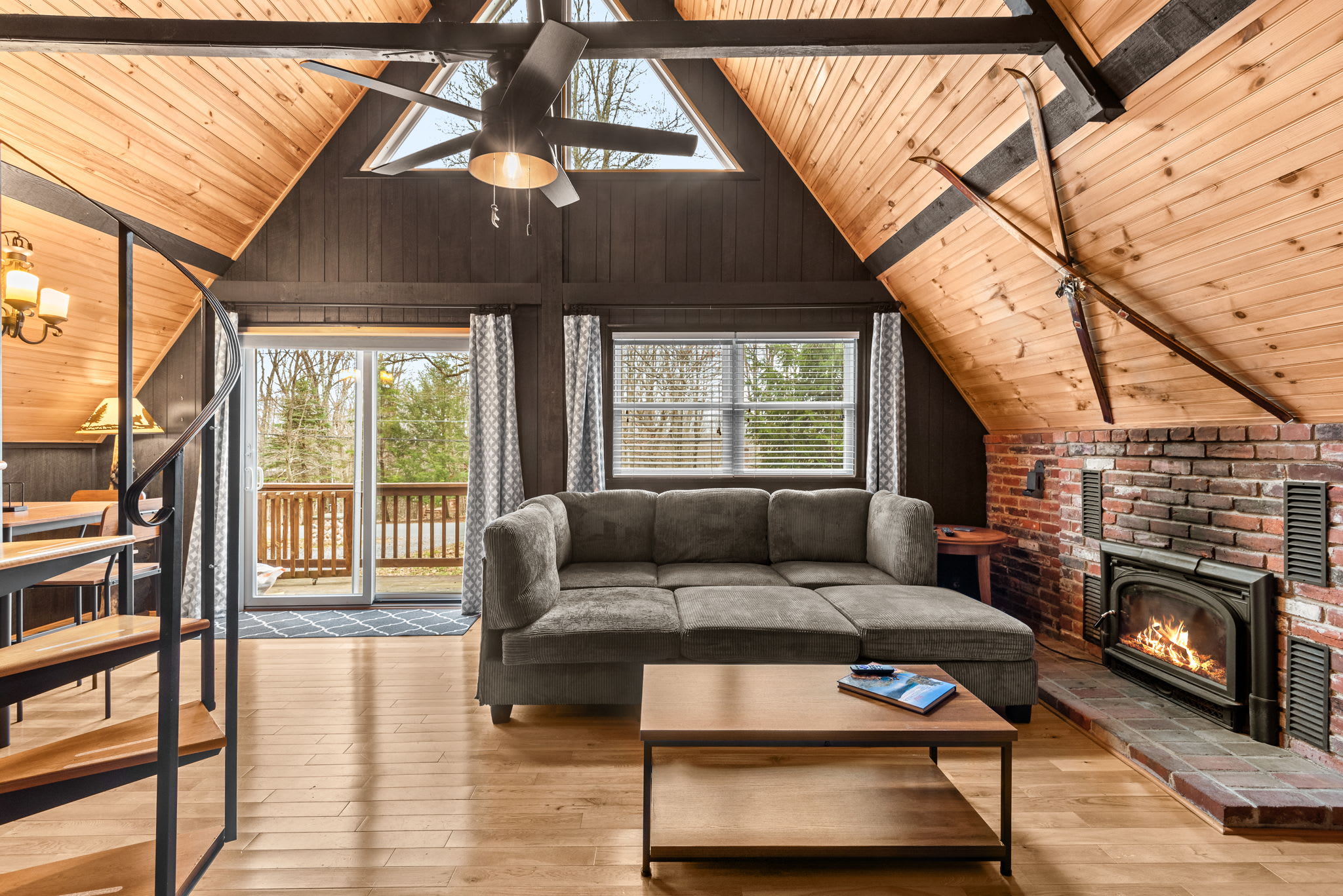 A cozy gathering space featuring a wood-burning brick fireplace, high ceilings, and an inviting sectional sofa.