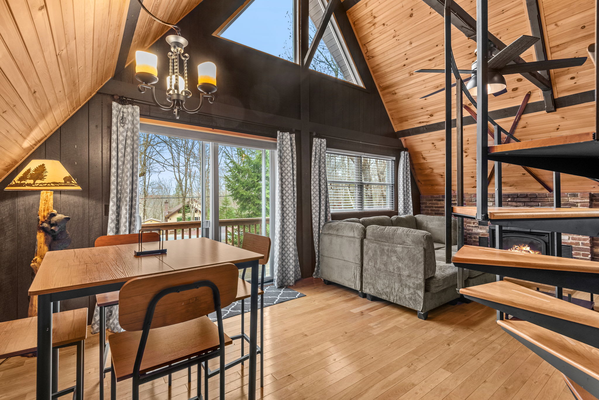A charming dining space with a high-top wooden table, stylish metal chairs, and a view of the surrounding trees through sliding glass doors.