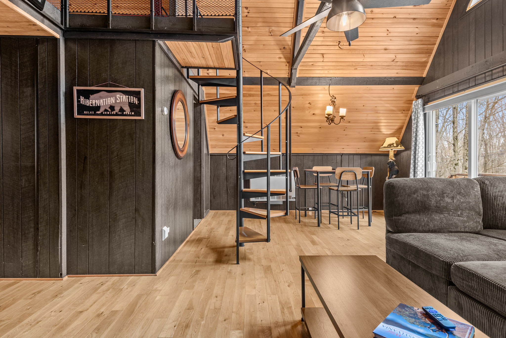  A stunning open-concept living space featuring a modern spiral staircase, wood-paneled ceilings, and cozy cabin décor.