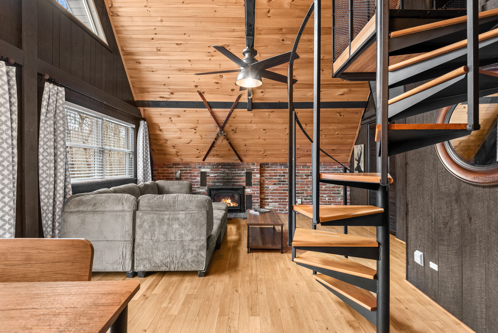 A stylish and inviting lounge area featuring a wood-burning fireplace, vaulted ceilings, and a modern spiral staircase.