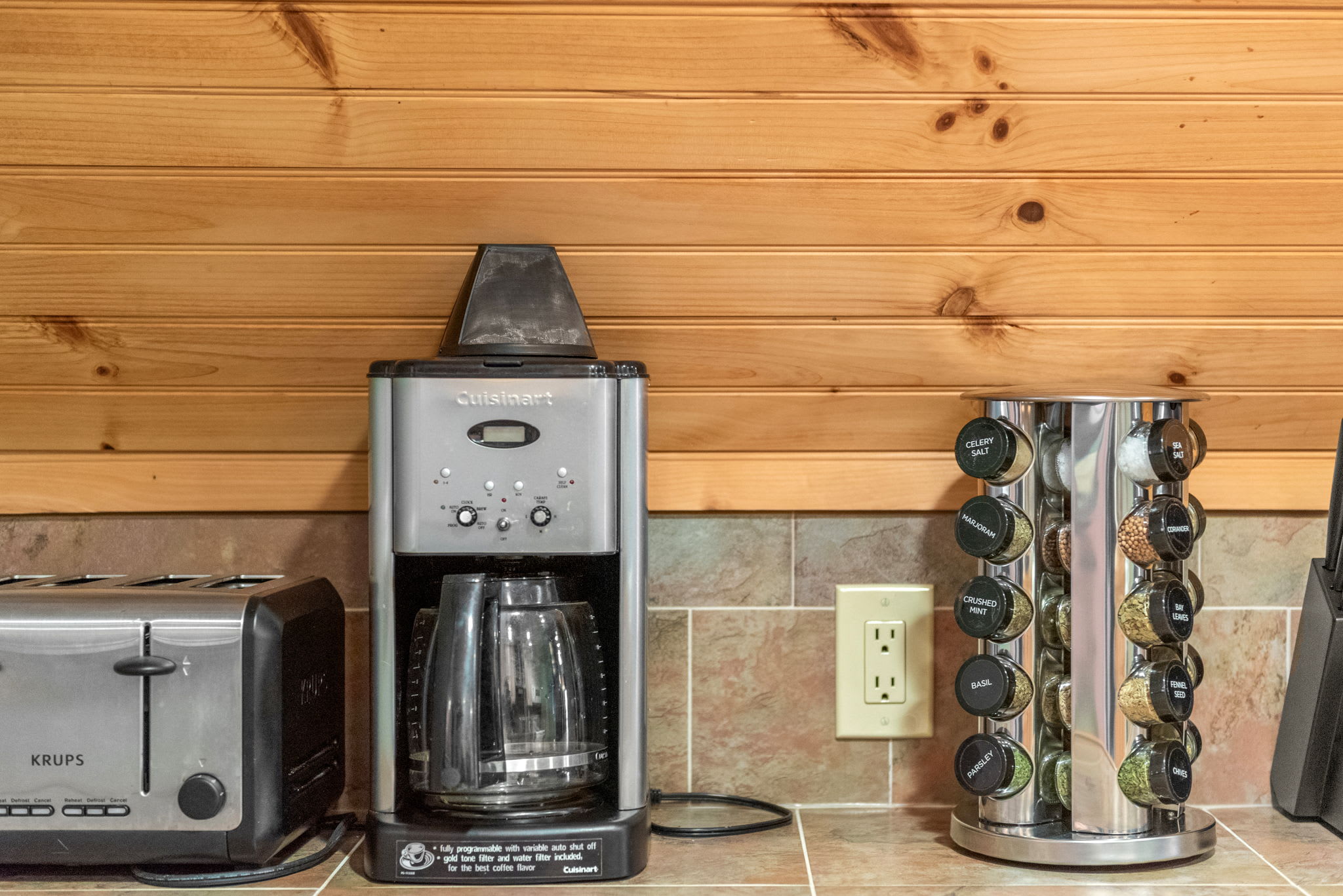 A well-stocked coffee bar with a Cuisinart coffee maker, Krups toaster, and a neatly arranged spice rack for guest convenience.