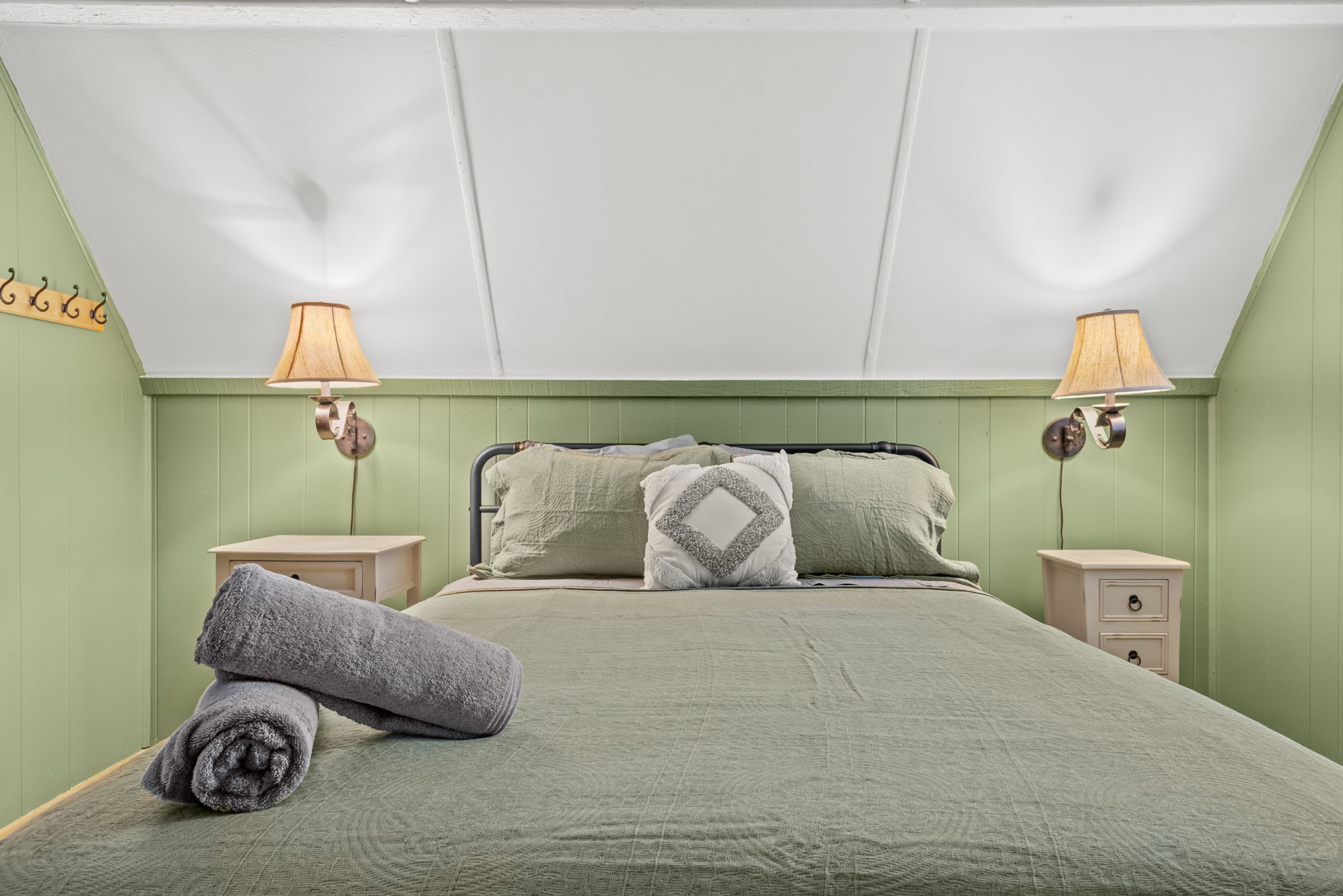 A serene and inviting bedroom featuring a soft green color palette, plush bedding, and warm bedside lighting.