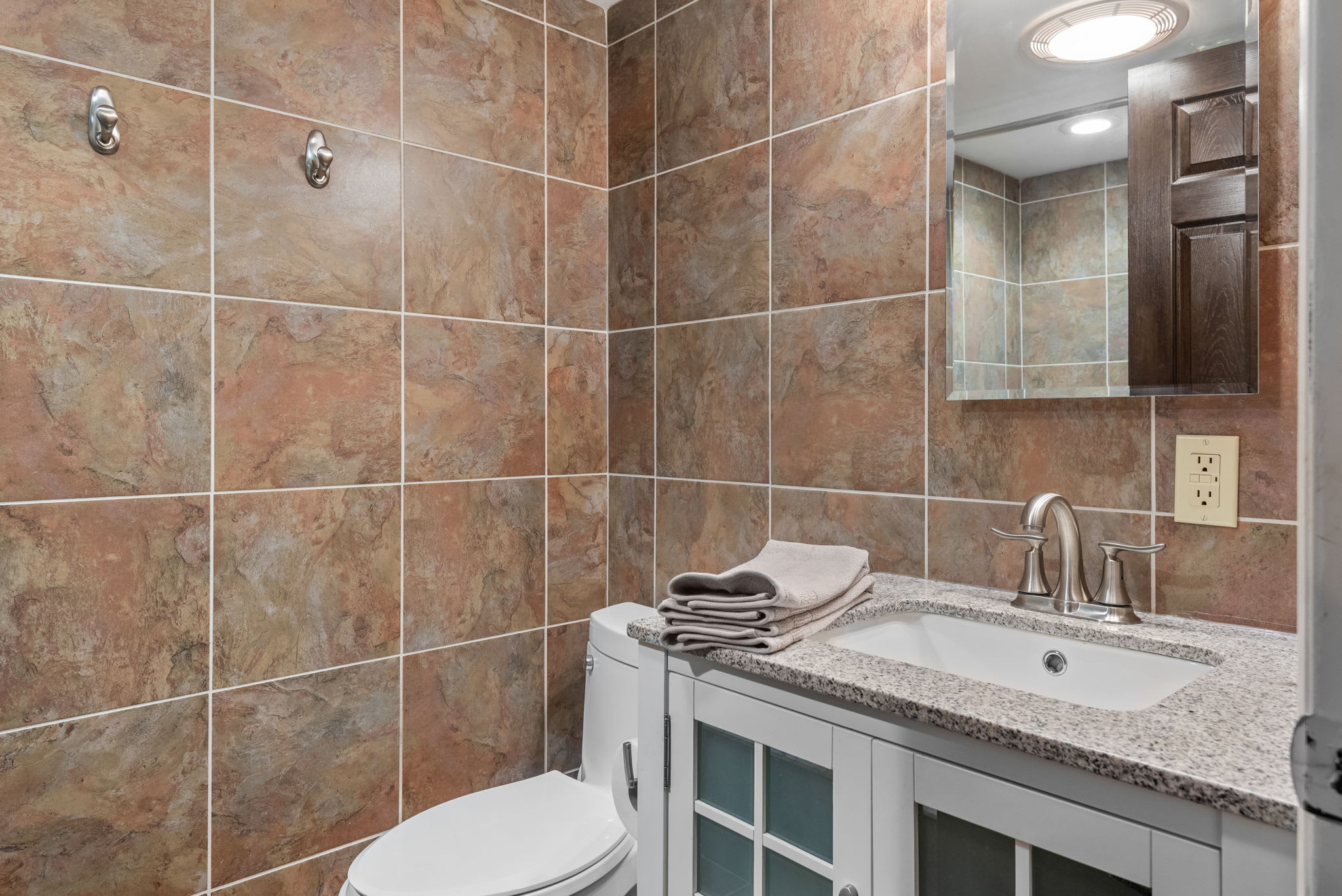 Stylish bathroom with stone-style tiles, granite countertop, and a sleek white vanity.