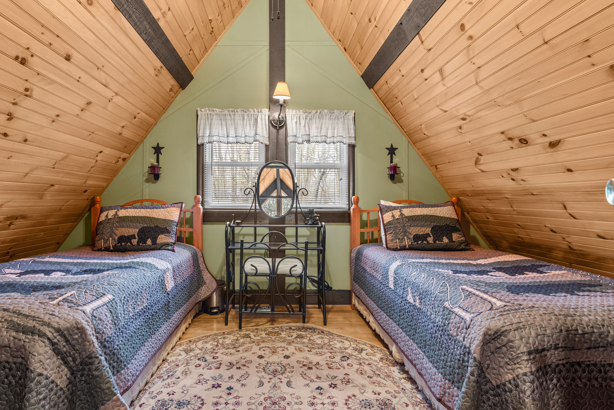 A charming loft bedroom with two twin beds, rustic bear-themed bedding, and a vintage vanity.