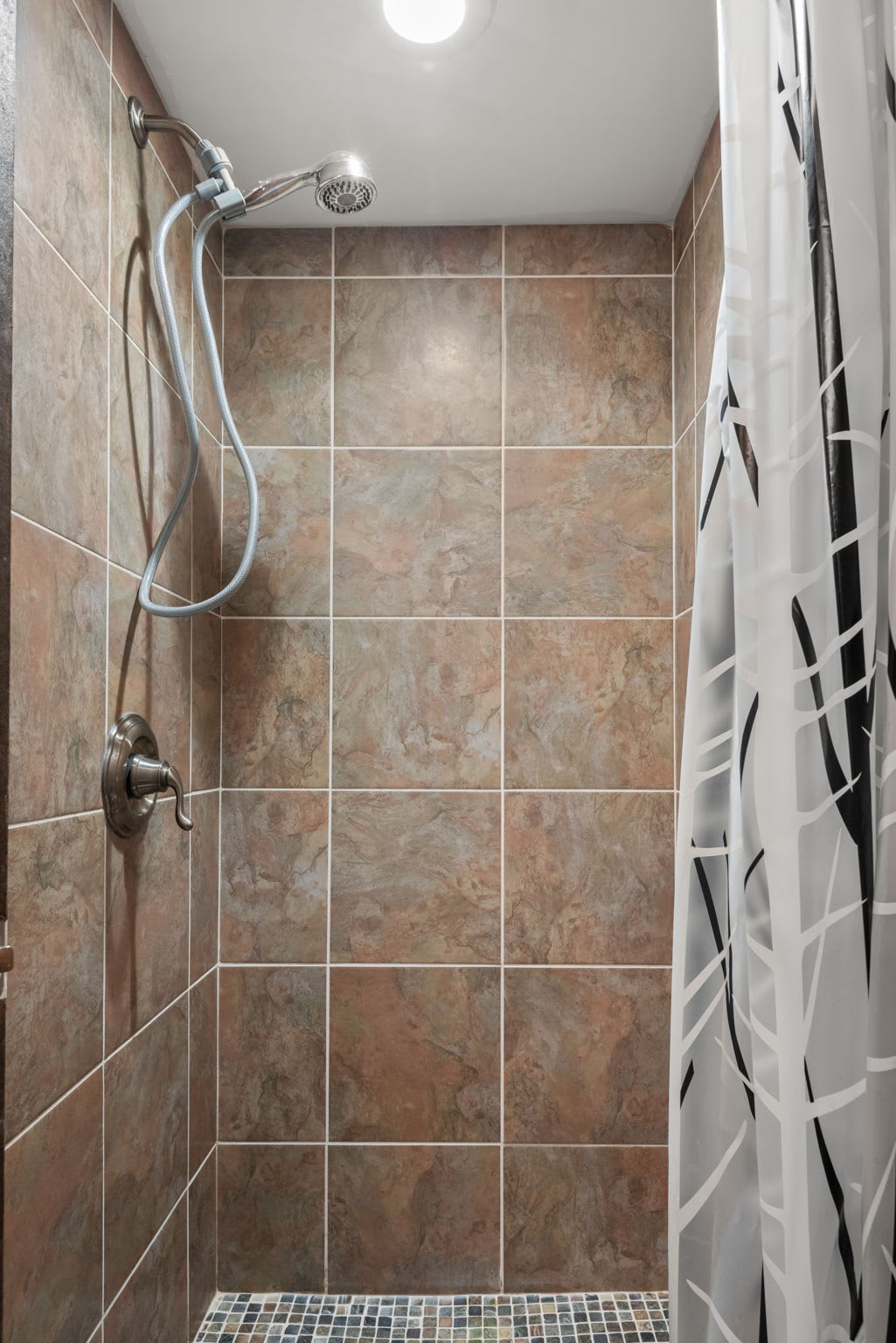 Spacious tiled shower with a rainfall-style showerhead and a modern curtain design.
