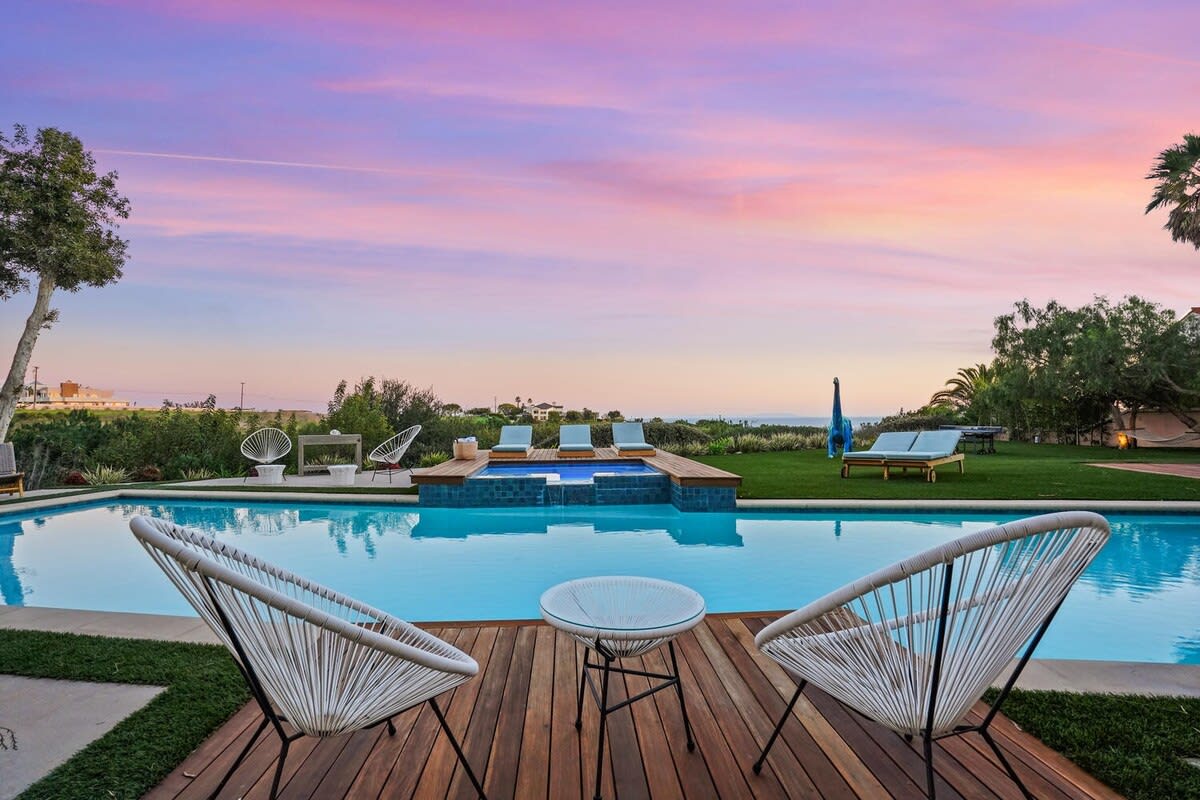 Chairs by the pool under a night sky painted with cotton candy hues.