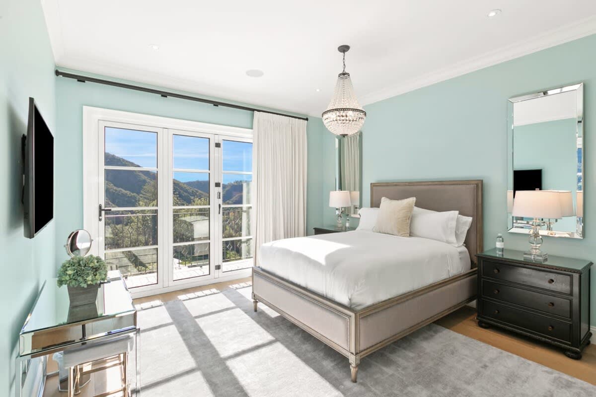 Guest bedroom with a King Bed accented with an elegant chandelier and views of Beverly Hills, hillside.