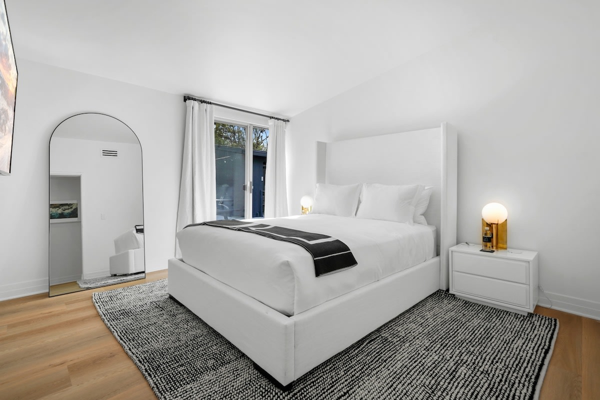 3rd guest bedroom with a linen queen size bed, beach style side tables, gold side lamps, blackout shades, Smart TV, white hotel style linens, large boucle performance rug and throw.