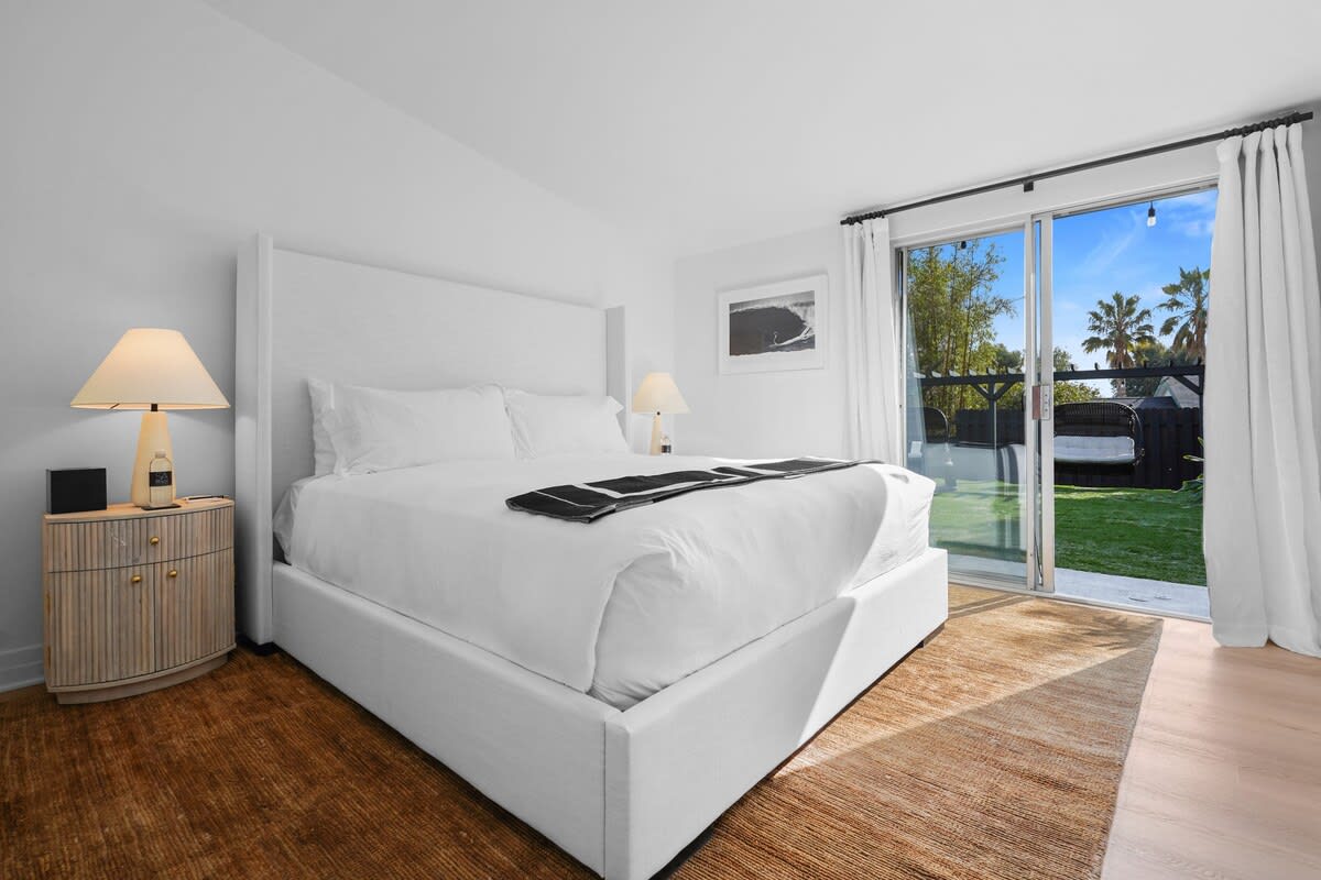 2nd guest bedroom with a linen king size bed, beach style side tables, stone side lamps, blackout shades, Smart TV, white hotel style linens and throw.