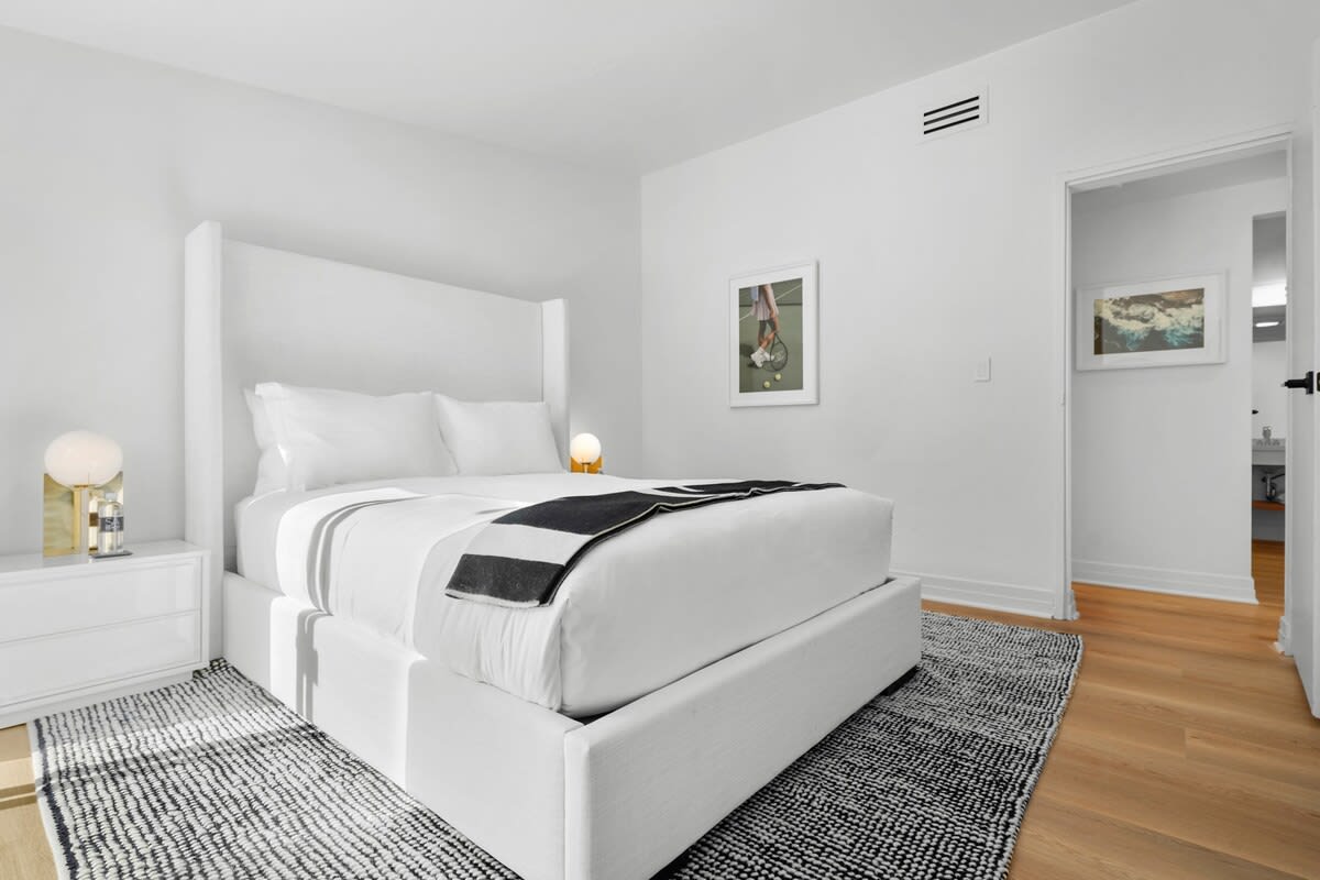 3rd guest bedroom with a linen queen size bed, beach style side tables, gold side lamps, blackout shades, Smart TV, white hotel style linens, large boucle performance rug and throw.