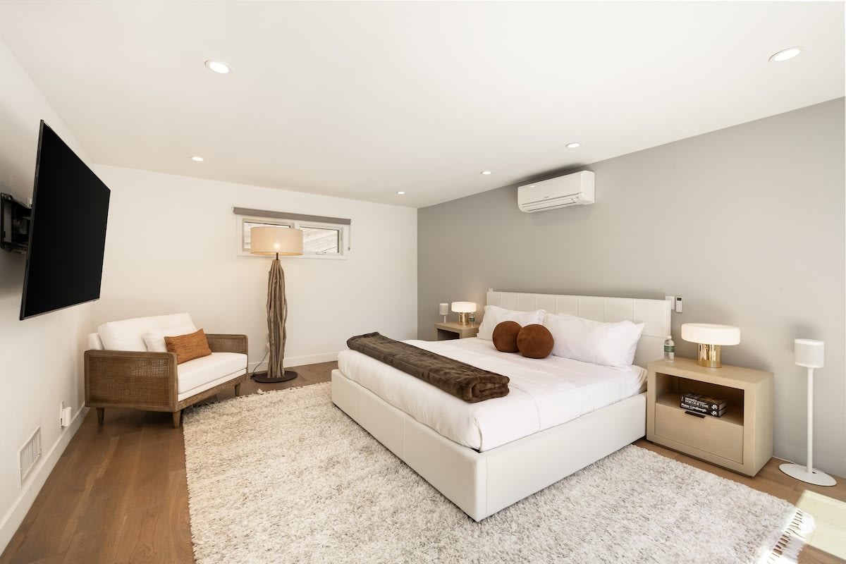 Spacious bedroom equipped with a smart TV, plush lounge chair, and luxurious linens.