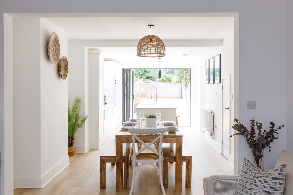 A large wooden dining table with bench seating for up to 8 guests sits between the kitchen and living room.